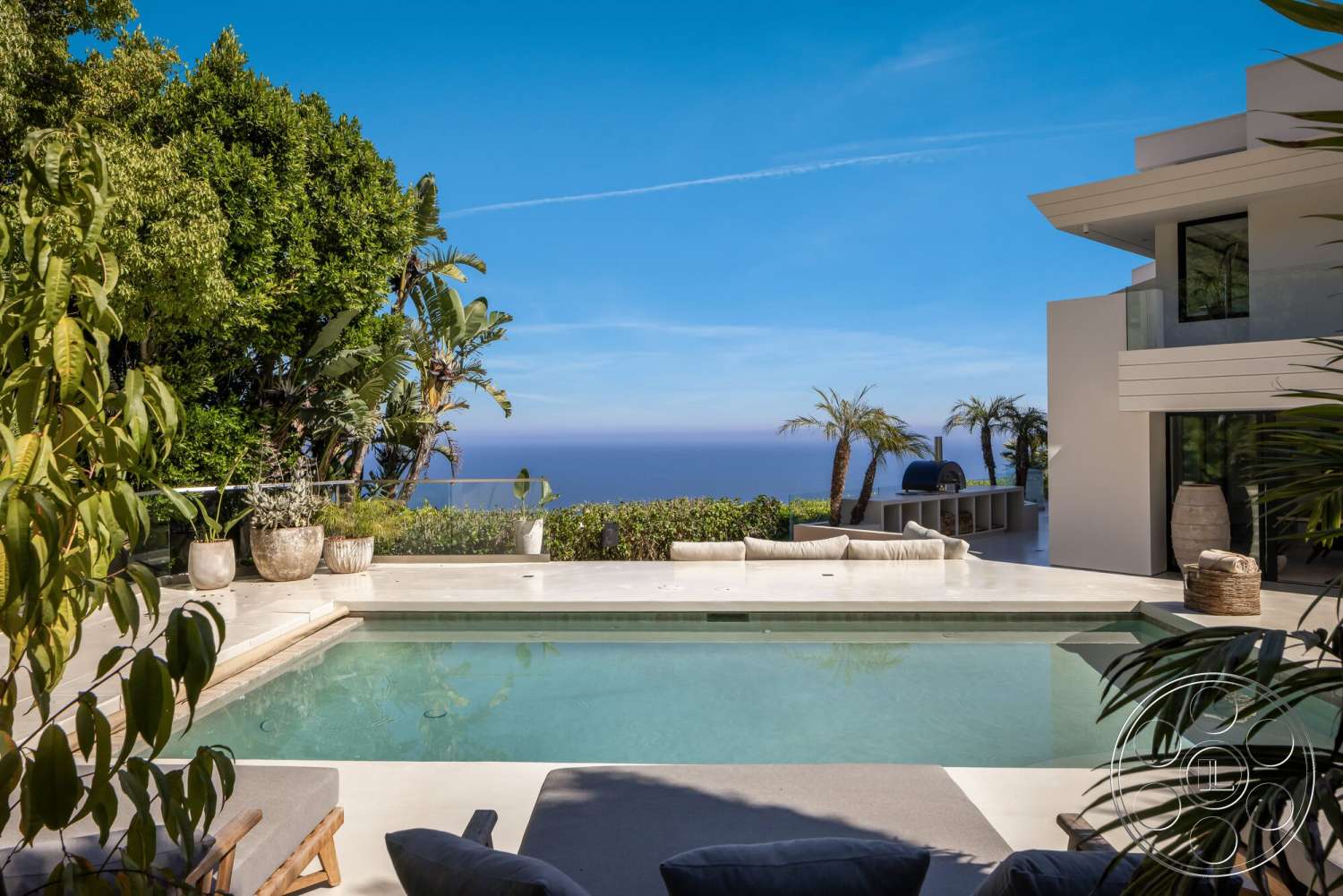 Modern 528 - glass railing, modern outdoor furniture, floor-to-ceiling windows, potted greenery, sunny coastal setting, rectangular pool, wooden lounge chairs, concrete patio flooring, concrete pool border, two-story contemporary home, open ocean view