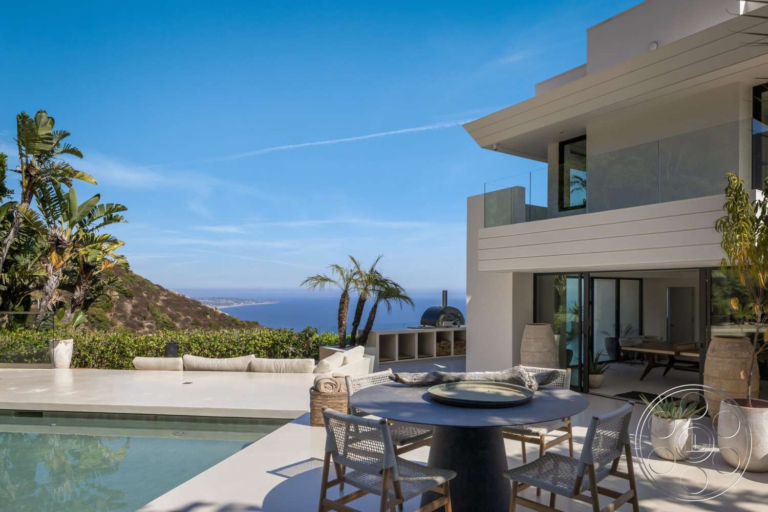 Modern 528 - exterior, outdoor seating area, rectangular swimming pool, floor-to-ceiling windows, ocean view, concrete patio flooring, modern minimalist architecture, palm tree landscaping, textured stone planters, glass balcony railings, landscaped hillside garden, al-fresco dining area, stone outdoor oven