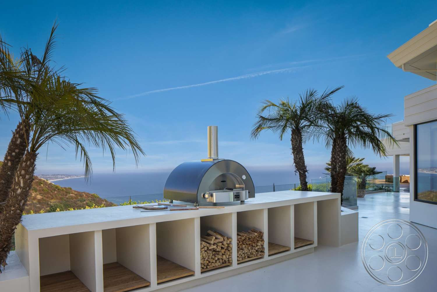 Modern 528 - exterior, palm trees, wood countertop, ocean view, hillside location, concrete patio flooring, modern outdoor kitchen, stainless steel pizza oven, wood storage cubby