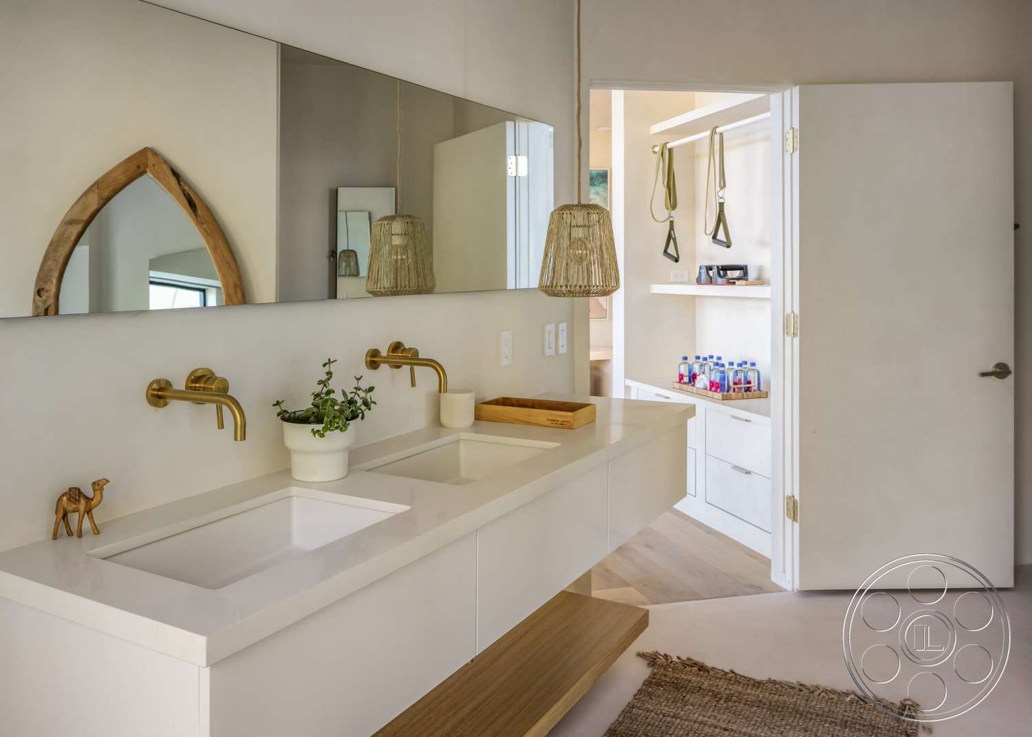 Modern 528 - light wood flooring, wood countertop, interior bathroom, neutral-toned area rug, white porcelain sinks, minimalist white cabinetry, hanging woven light fixtures, golden brass faucets, natural wood trim mirror, light beige wall finish, simple decorative plant arrangement, open door entrance to storage