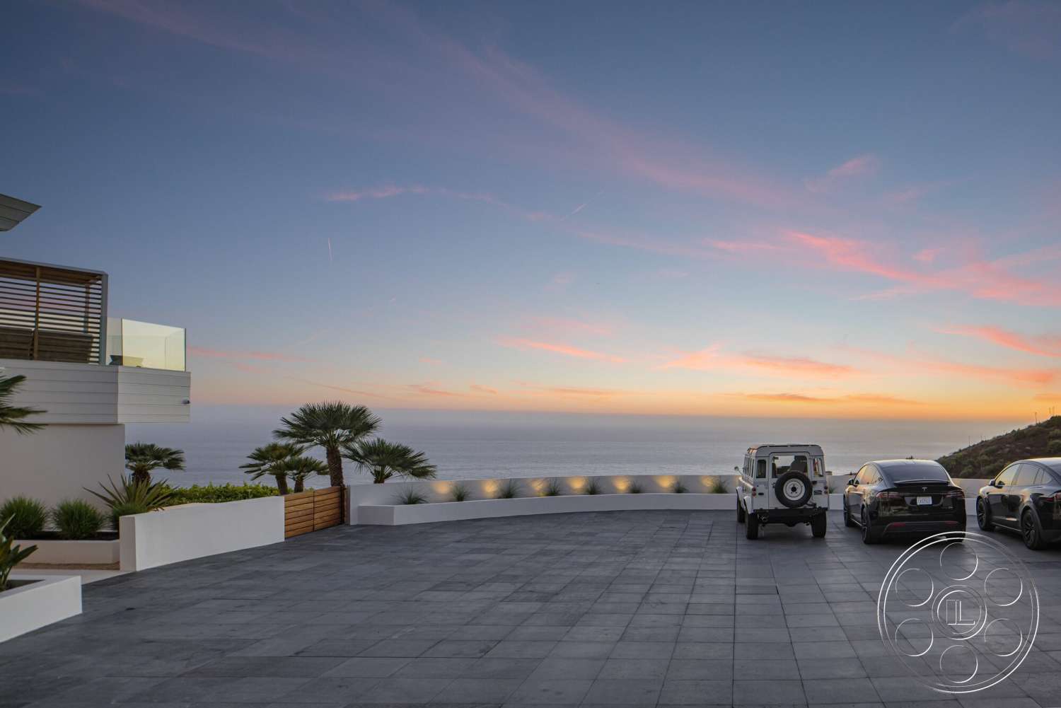 Modern 528 - exterior, white stucco walls, modern architectural style, concrete driveway, textured concrete surface, glass balcony railing, landscape palm trees, ocean view setting, horizontal wood slat screen, sunset skyline, curved landscape borders