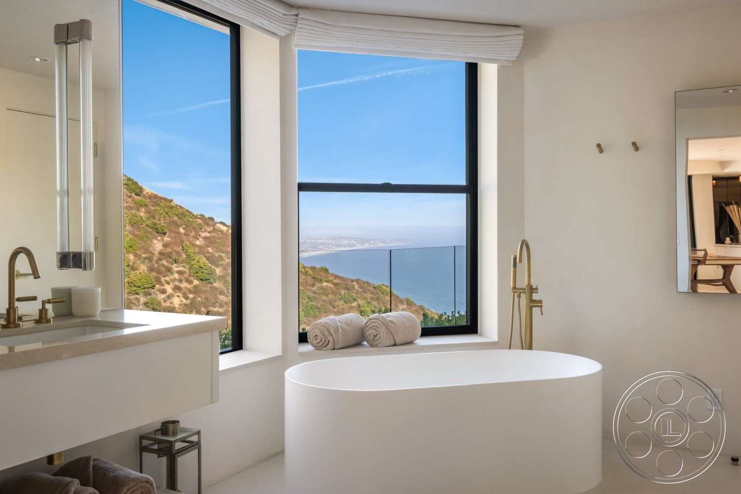 Modern 528 - minimalist design, floor-to-ceiling windows, mountain backdrop, clear blue sky, white freestanding bathtub, contemporary lighting fixtures, gold faucet fixtures, interior modern bathroom, light-colored plaster walls, exterior ocean view, stone countertop vanity, large towel rolls, nature-inspired setting