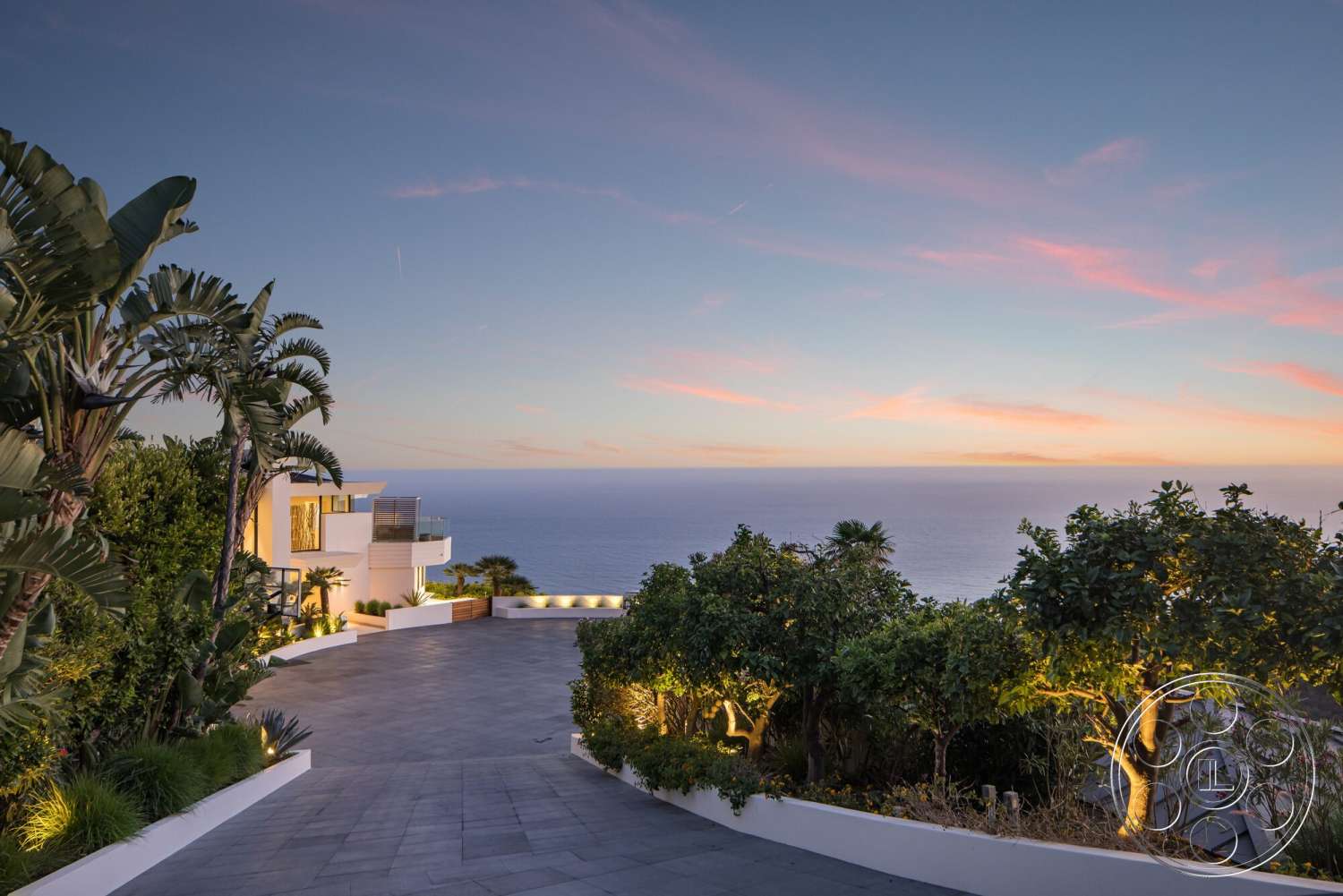 Modern 528 - exterior, white stucco walls, floor-to-ceiling windows, contemporary architecture, balcony with railing, curved driveway, outdoor lighting features, tropical landscaping, sunset sky, sea view, planted garden beds, terraced landscaping, modern home design, lush green foliage, slate driveway