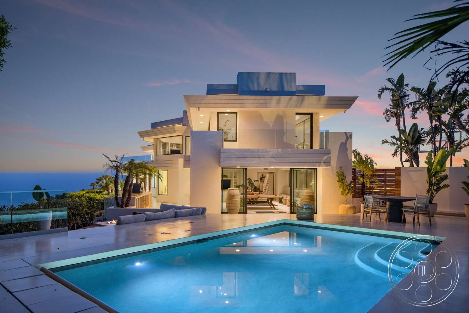 Modern 528 - exterior, white stucco walls, large glass sliding doors, rectangular swimming pool, open-plan layout, outdoor dining table, flat roof design, palm trees landscaping, textured concrete patio flooring, two-story modern home, floating concrete steps, ocean view setting, glass railing around pool area, sunset sky backdrop