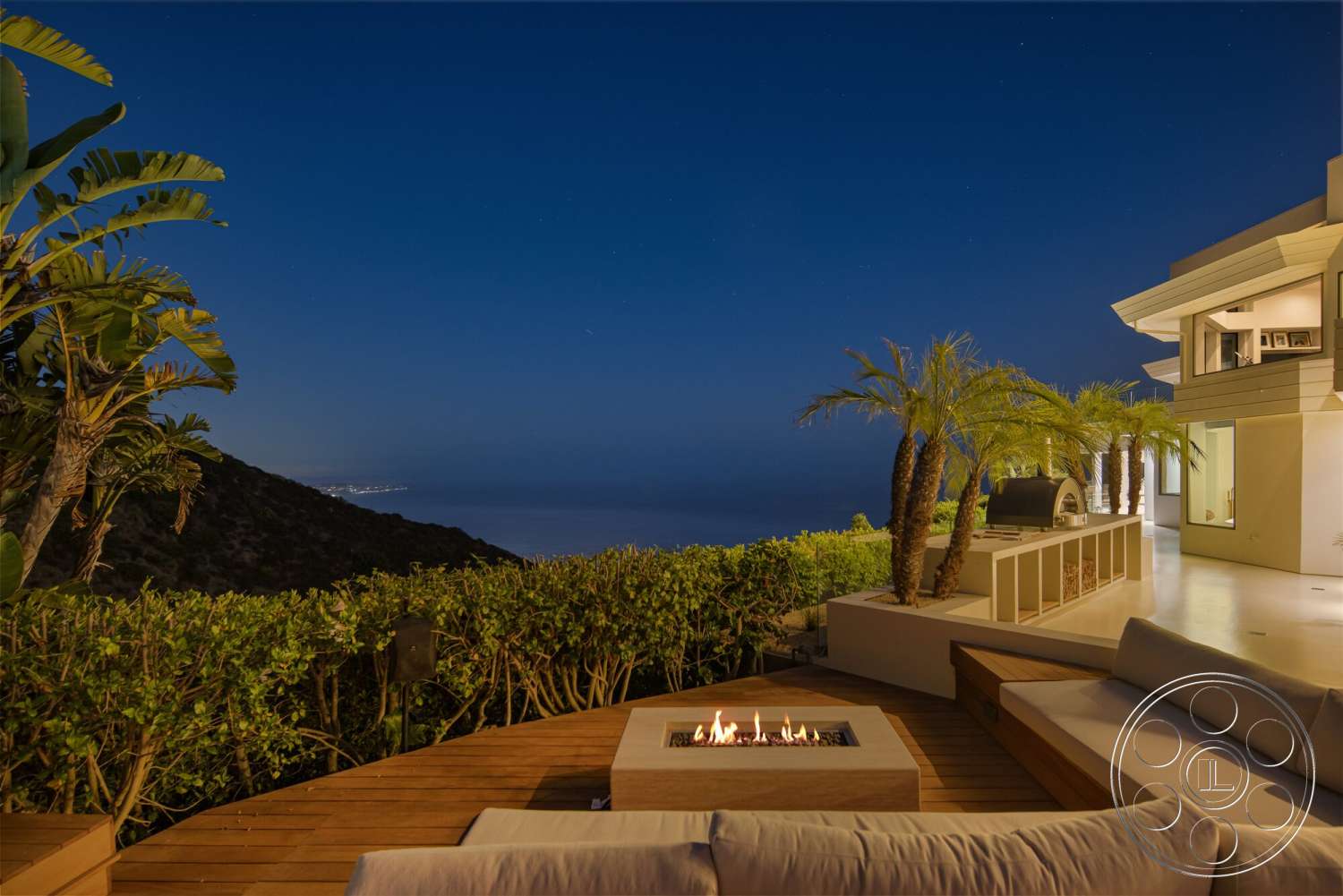 Modern 528 - exterior, flat roof, glass sliding doors, outdoor dining area, ocean view, white painted walls, concrete patio floor, wooden deck patio, palm trees landscaping, modern hillside home, rectangular fire pit, built-in outdoor seating