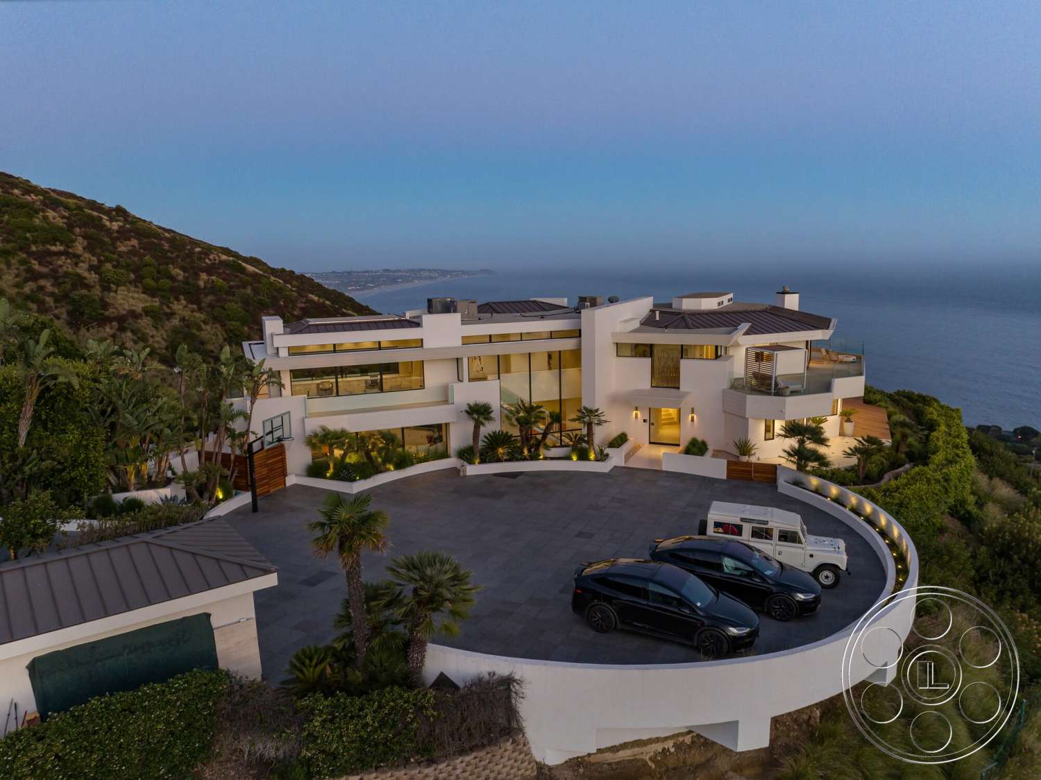 Modern 528 - exterior, flat roof, large glass windows, modern architectural style, ocean view, concrete driveway, mountain backdrop, garden patio, outdoor terrace, veranda, metal roofing, curved architectural forms, smooth white stucco walls, stone landscape border, trophy palm trees, dimensional pavers, multiple vehicle parking, landscaped surrounds