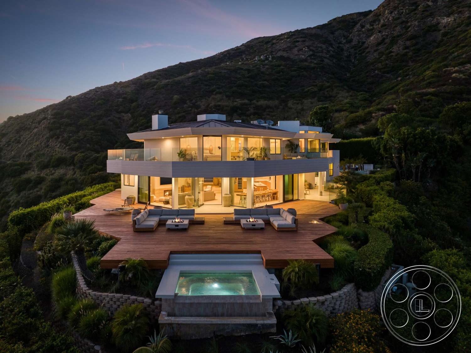 Modern 528 - exterior, modern architecture, floor-to-ceiling windows, hillside location, landscaped garden setting, open concept living area, wood deck flooring, glass balcony railing, panoramic mountain views, multiple outdoor seating areas, curved house, concrete hot tub border