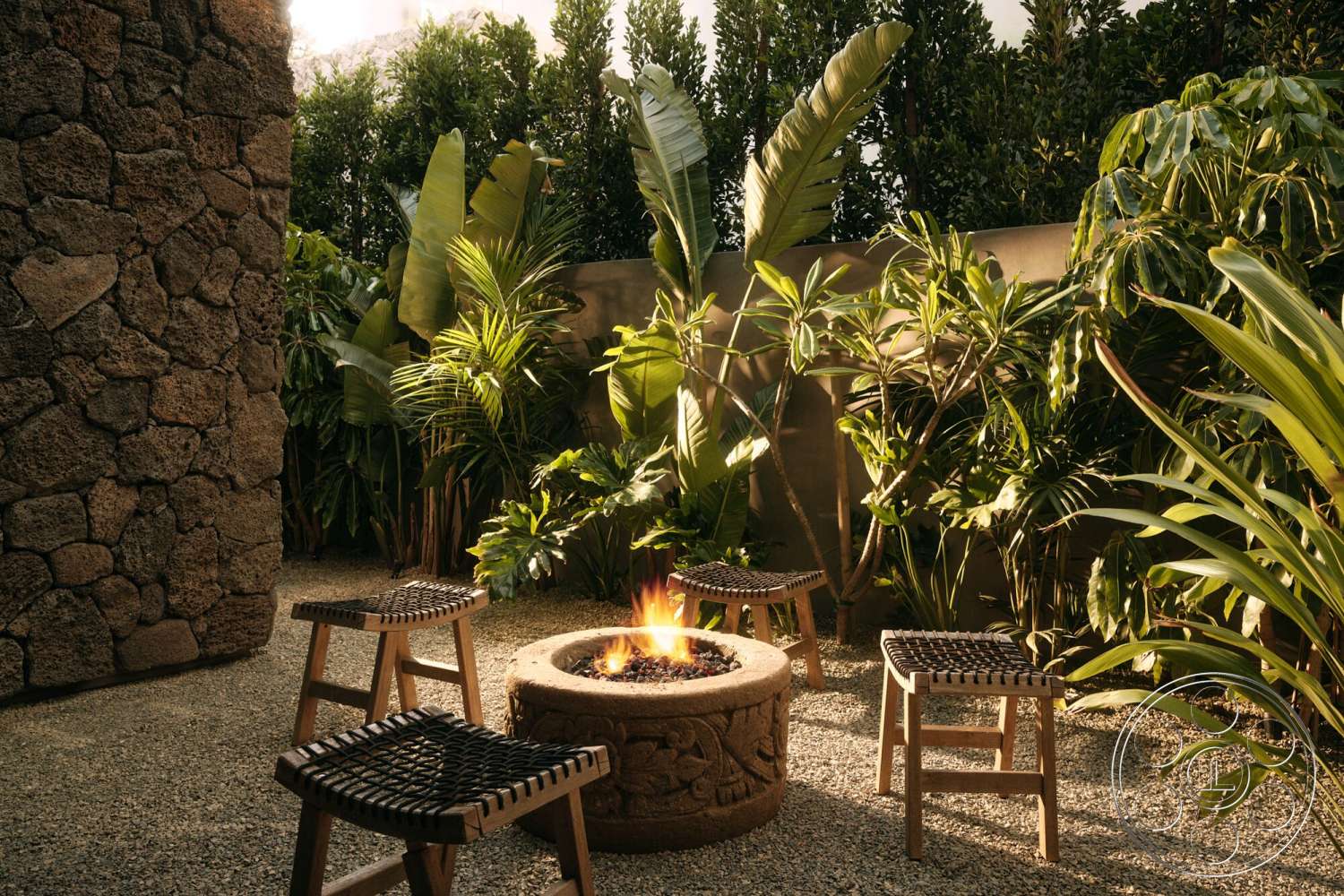 Modern 530 - exterior, natural stone elements, green hedges, lush tropical landscaping, round fire pit, gravel patio flooring, rough stone wall, decorative stone fire pit surround, woven wood outdoor stools, tall leafy plants
