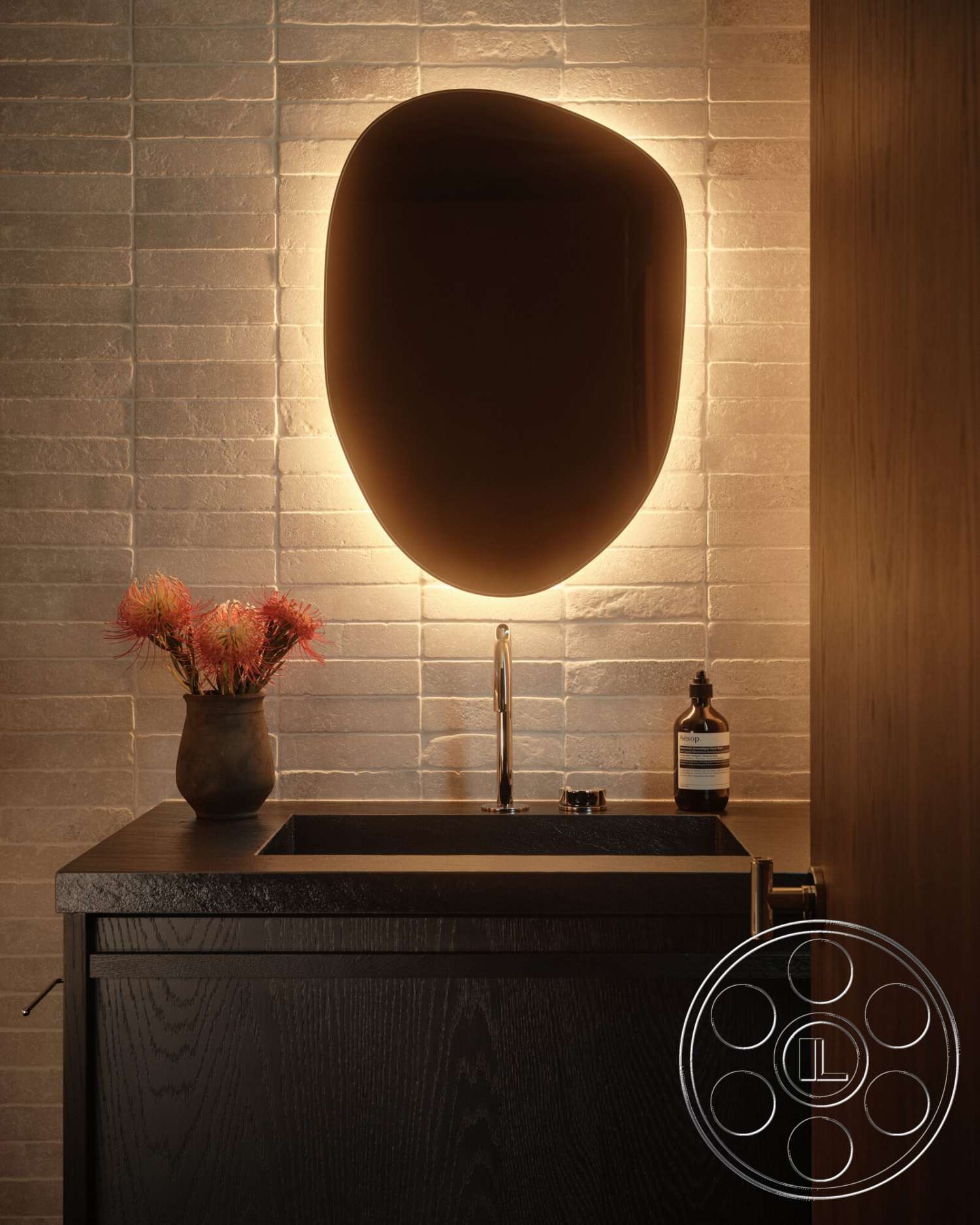 Modern 530 - minimalist design elements, soft ambient lighting, black stone countertop, decorative vase with flowers, textured stone wall tiles, solid wood vanity with dark finish, rounded wall-mounted mirror, sleek metal faucet, wooden door with simple design