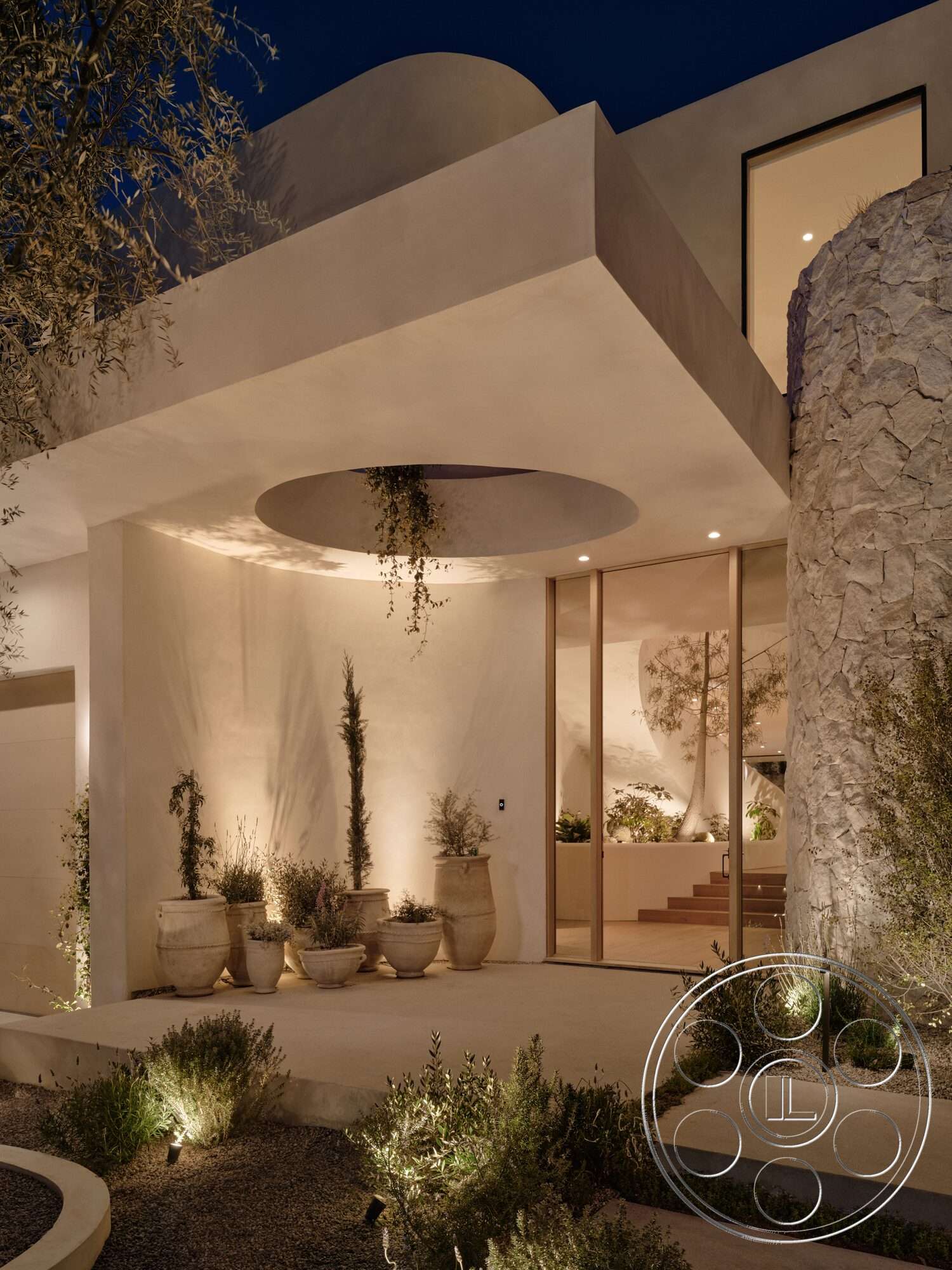 Modern 531 - exterior, floor-to-ceiling windows, contemporary design elements, textured plaster walls, desert setting, stone feature wall, minimalist entrance, concrete patio flooring, landscape lighting features, planter pots with greenery, rounded architectural forms, soft evening lighting, interior stairs leading inside