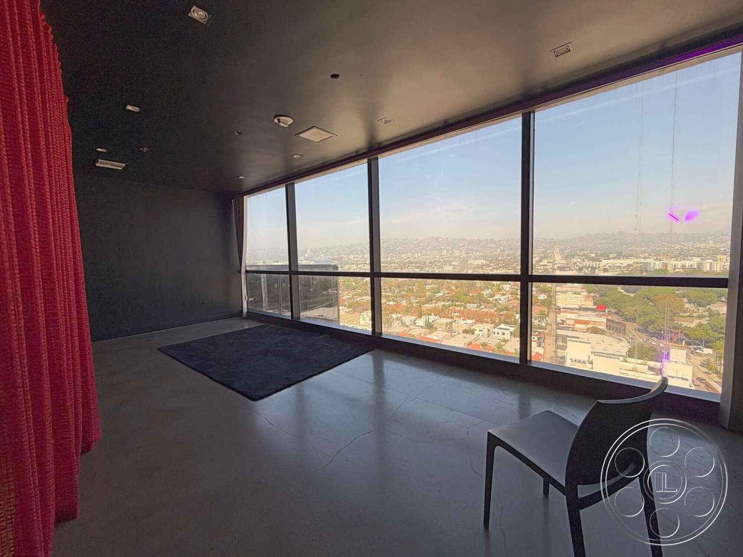 Wilshire Penthouse - natural light, open floor plan, floor-to-ceiling windows, simple geometric shapes, contemporary interior, minimalist interior design, exposed concrete flooring, black painted ceiling, urban city skyline view, curtains in rich red fabric, modern high-rise apartment