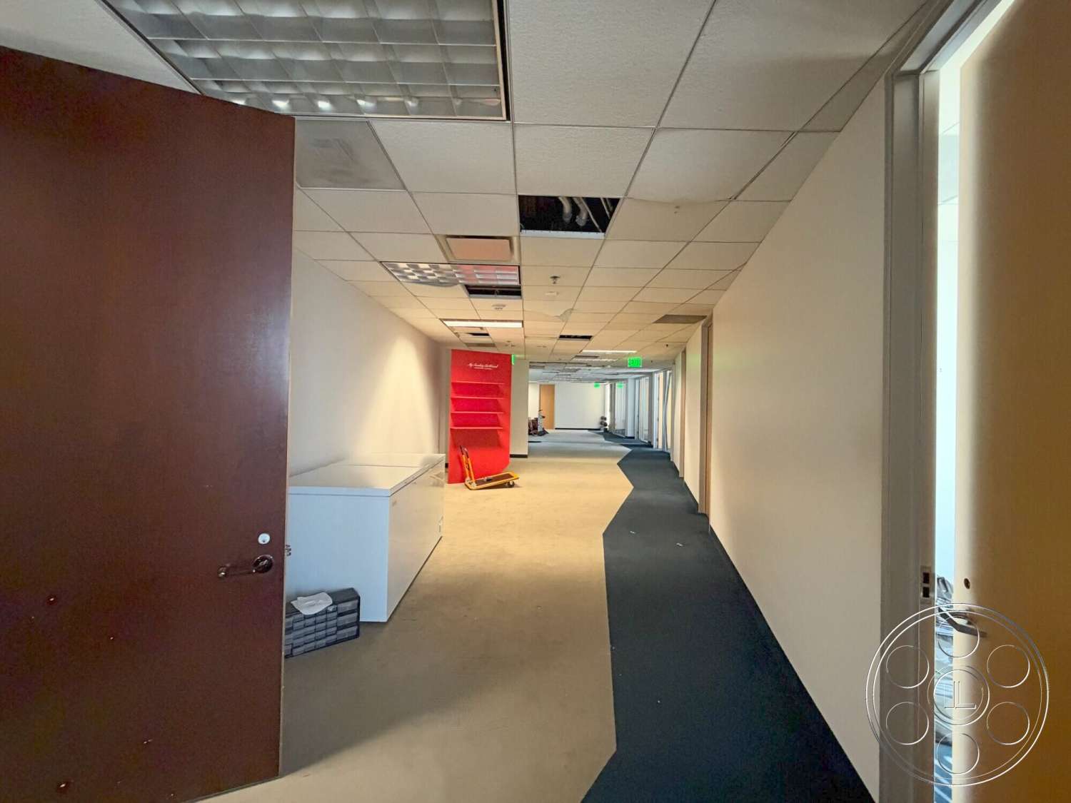 Wilshire Penthouse - wooden door, carpet flooring, open office layout, interior hallway, painted drywall walls, drop ceiling tiles, clear glass window frames, red shelving unit, LED panel lights, off-white wall color