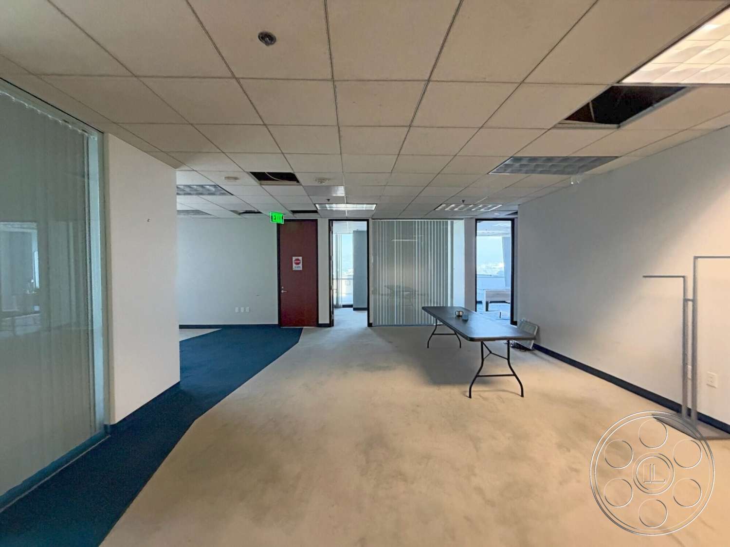 Wilshire Penthouse - office chair, glass partition walls, interior office space, drop ceiling tiles, carpet office flooring, metal folding table, interior doorway, jetted window view, unfinished ceiling area, walls with white painted finish, blue carpet accent, door with wood finish