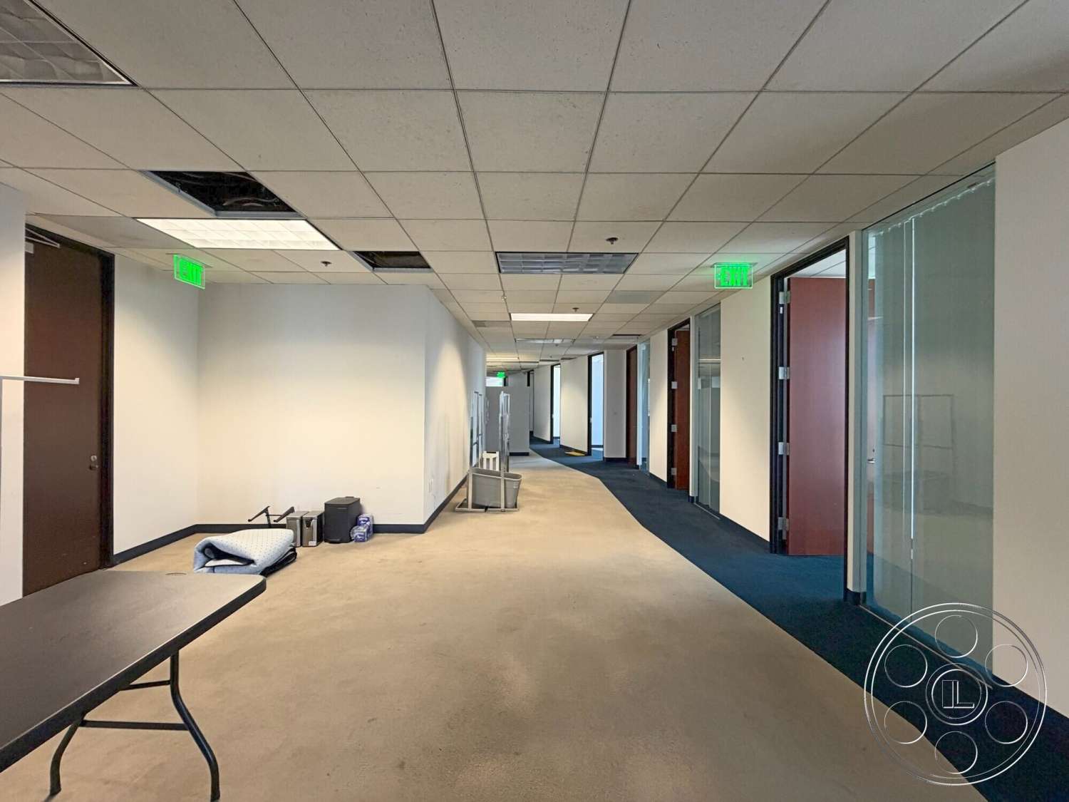 Wilshire Penthouse - track lighting, carpet flooring, glass partition walls, interior hallway, emergency exit signs, drywall painted white walls, dropped ceiling tiles, door frames with dark wood finish, office door hardware