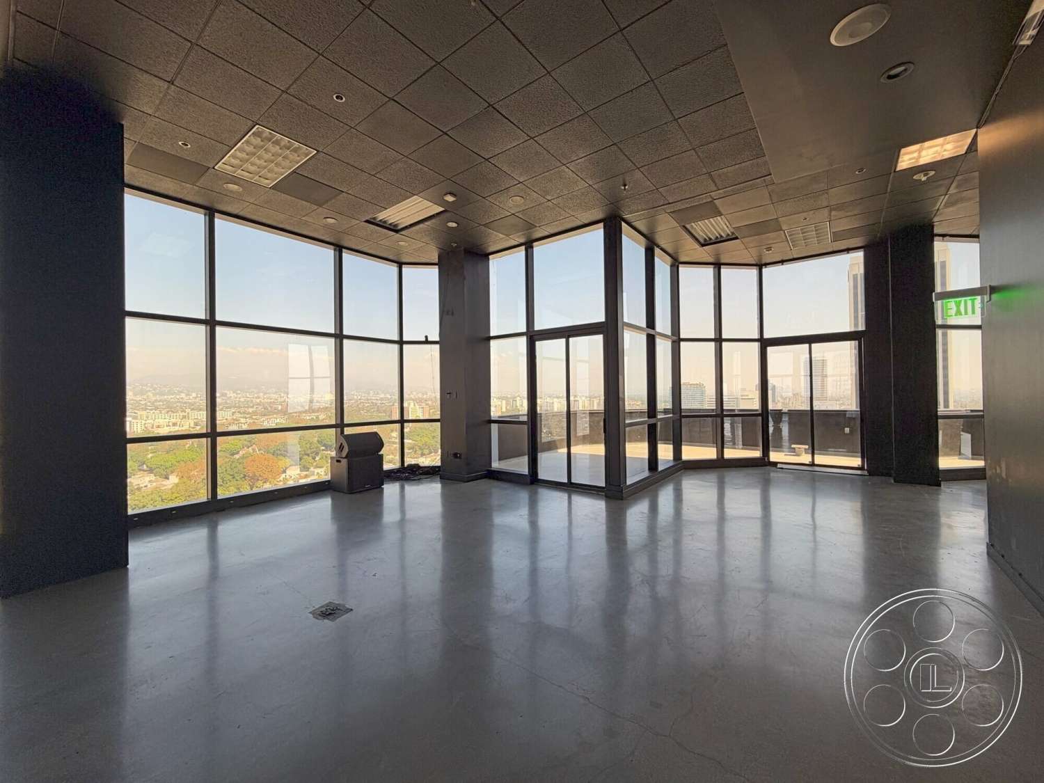 Wilshire Penthouse - exterior, minimalist design, open floor plan, concrete flooring, floor-to-ceiling windows, city skyline view, industrial ceiling tiles, modern office space, urban high-rise setting, corner office layout