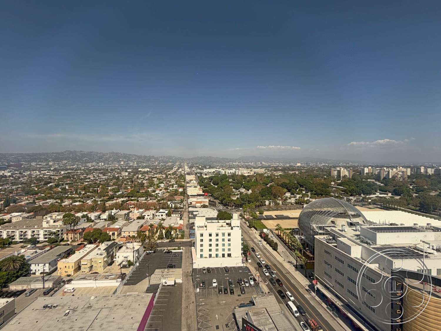 Wilshire Penthouse - urban landscape, urban rooftop, city skyline view, multi-story buildings, downtown area, distant mountain backdrop, parking lot surface, flat roof structures, concrete buildings, paved streets, greenery along roadways, residential neighborhood layout