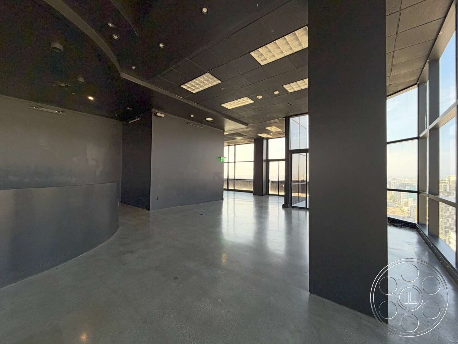 Wilshire Penthouse - open floor plan, polished concrete flooring, floor-to-ceiling windows, urban skyline view, curved wall design, dark painted walls, modern office space, ample natural light, drop ceiling with recessed lights