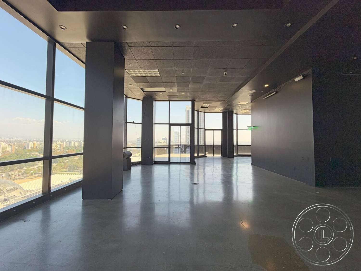 Wilshire Penthouse - floor-to-ceiling windows, modern architectural style, urban skyline view, black painted walls, open floor plan interior, high-rise building interior, commercial space design, exposed concrete floors, grid ceiling tiles