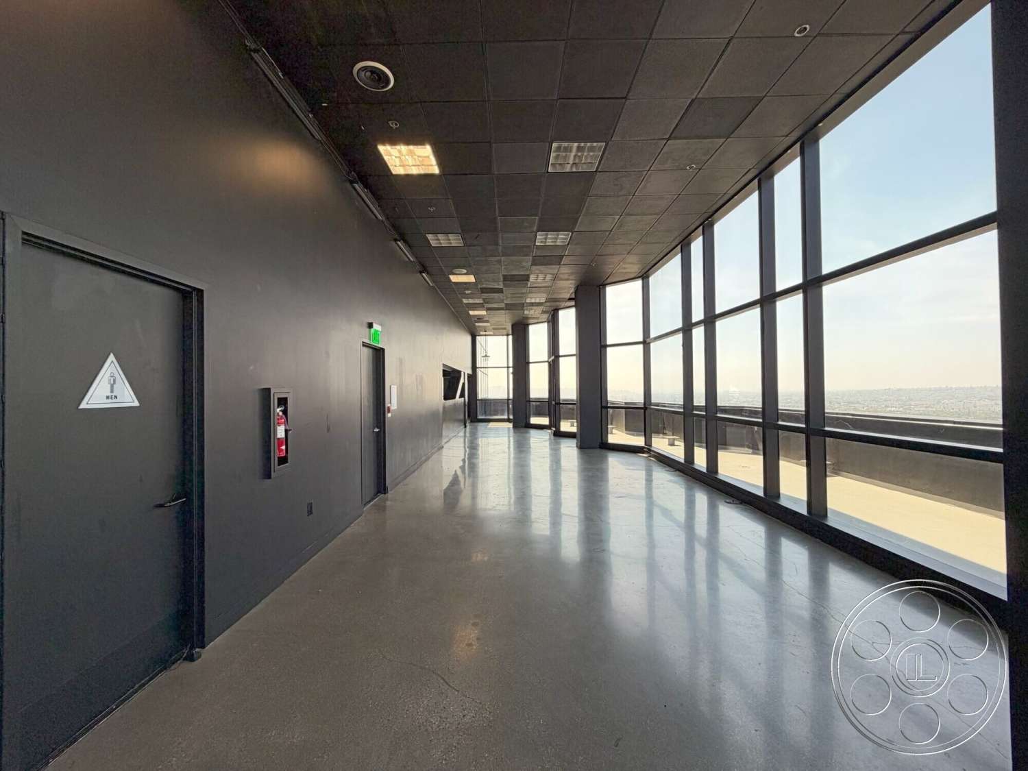 Wilshire Penthouse - exterior, polished concrete flooring, floor-to-ceiling windows, urban skyline view, black painted walls, square ceiling tiles, minimalist interior design, open corridor layout