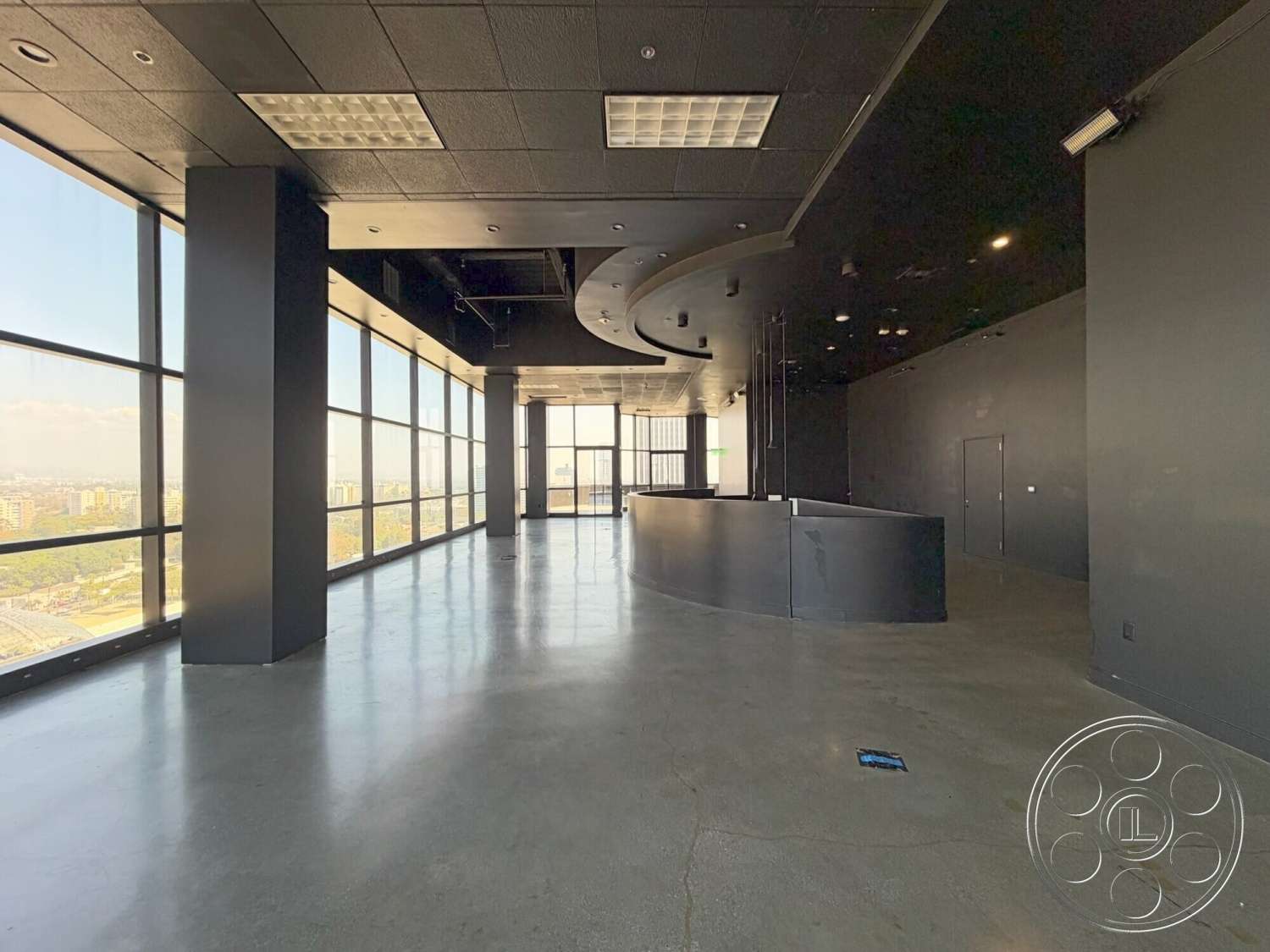 Wilshire Penthouse - minimalist design, polished concrete floor, floor-to-ceiling windows, modern architectural style, urban skyline view, open floor layout, curved reception desk, black ceiling tiles