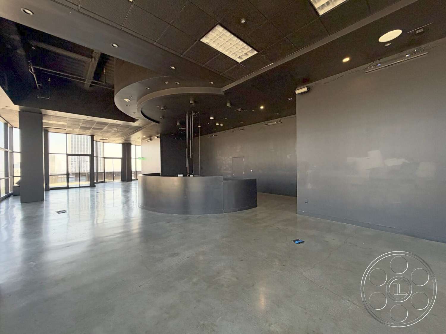 Wilshire Penthouse - open floor plan, polished concrete flooring, floor-to-ceiling windows, exposed ductwork, recessed lighting fixtures, modern minimalist design, urban high-rise setting, curved bar counter, black ceiling tiles