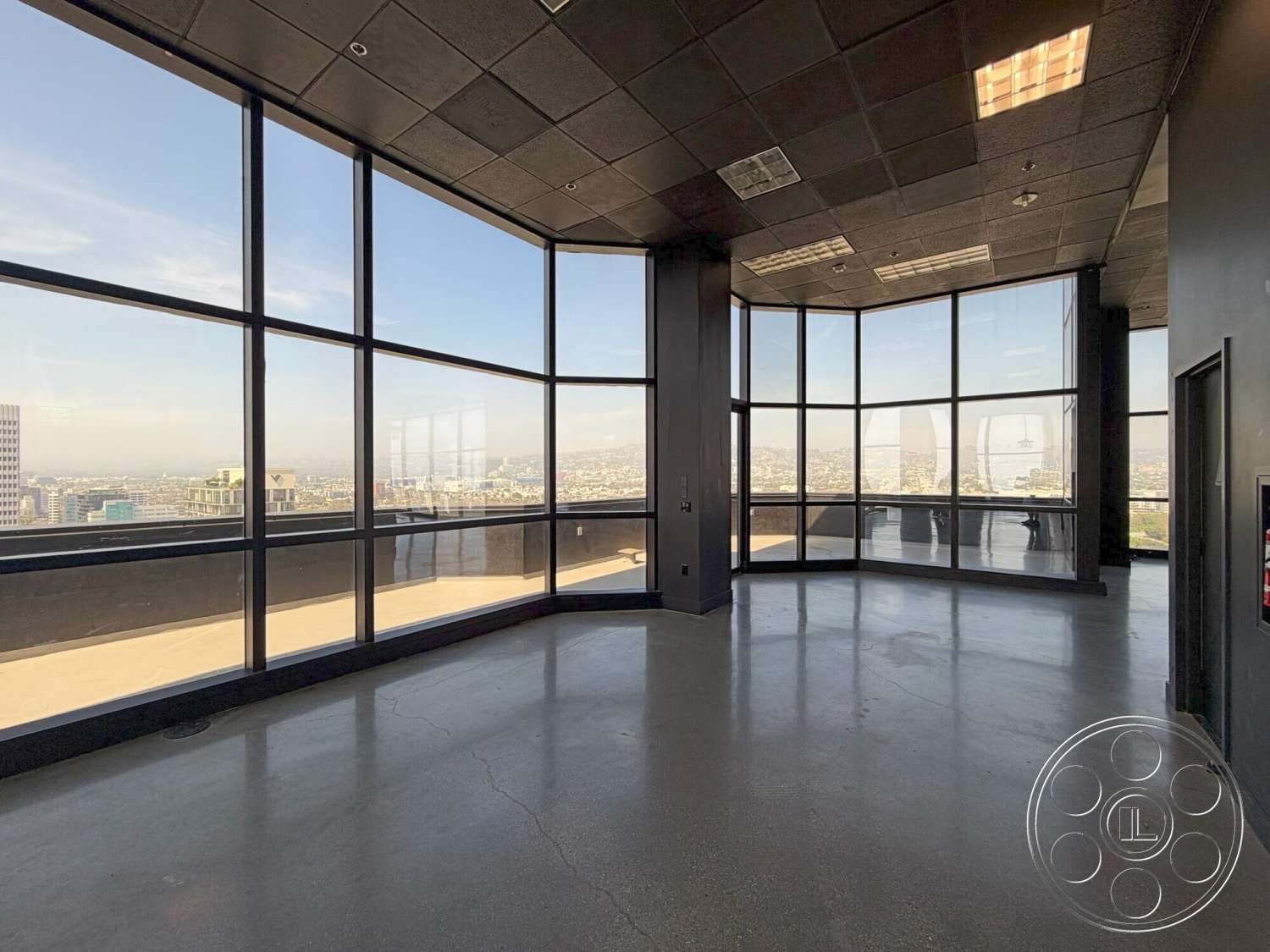 Wilshire Penthouse - open floor plan, polished concrete flooring, floor-to-ceiling windows, urban skyline view, modern minimalist design, industrial style architecture, corner office layout, steel window frames, black ceiling tiles