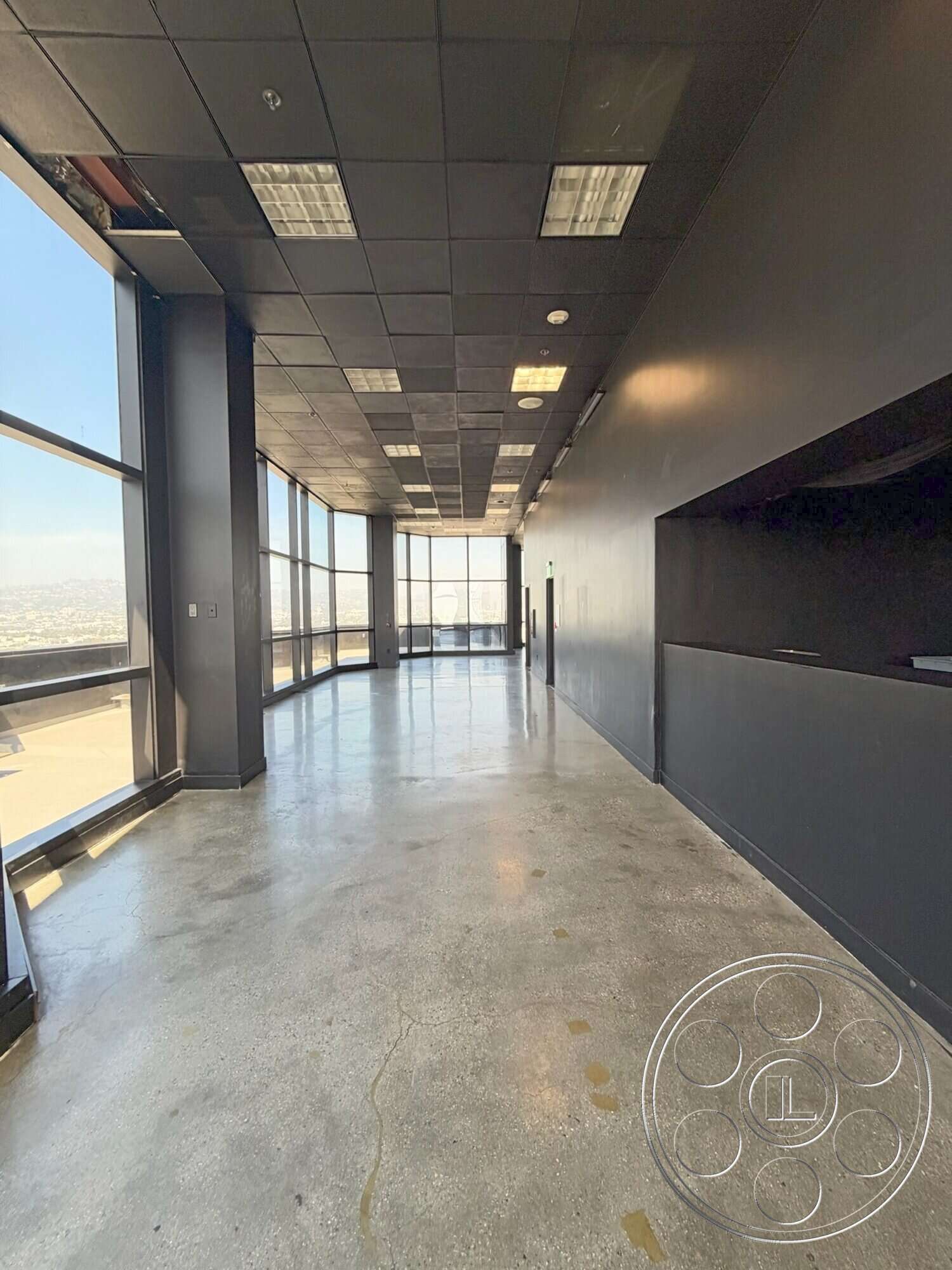 Wilshire Penthouse - open floor plan, polished concrete flooring, black painted walls, urban city view, drop ceiling with fluorescent lighting, structural glass windows