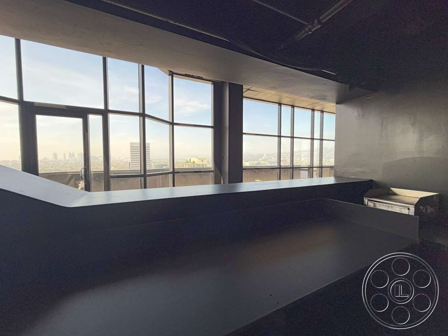 Wilshire Penthouse - open floor plan, smooth wall finish, panoramic city skyline view, steel frame windows, black concrete countertop, high-rise urban setting