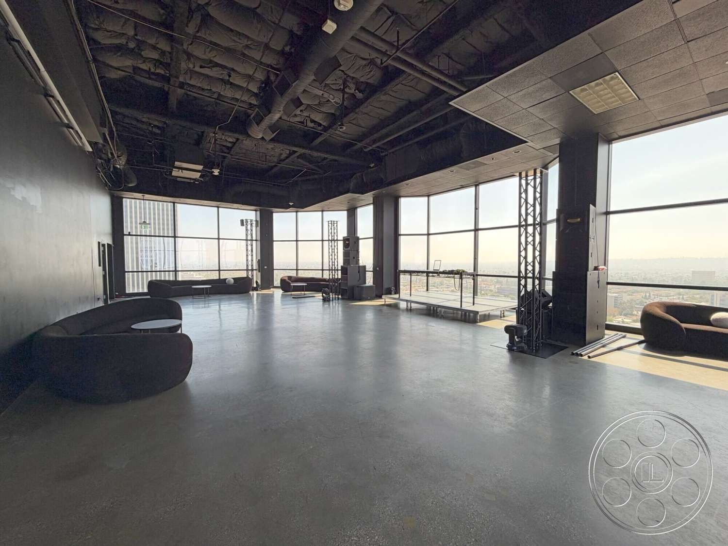 Wilshire Penthouse - minimalist decor, open layout, modern design, concrete flooring, industrial style, city skyline view, large floor-to-ceiling windows, dark wall treatment, exposed black ceiling design, soft curved seating