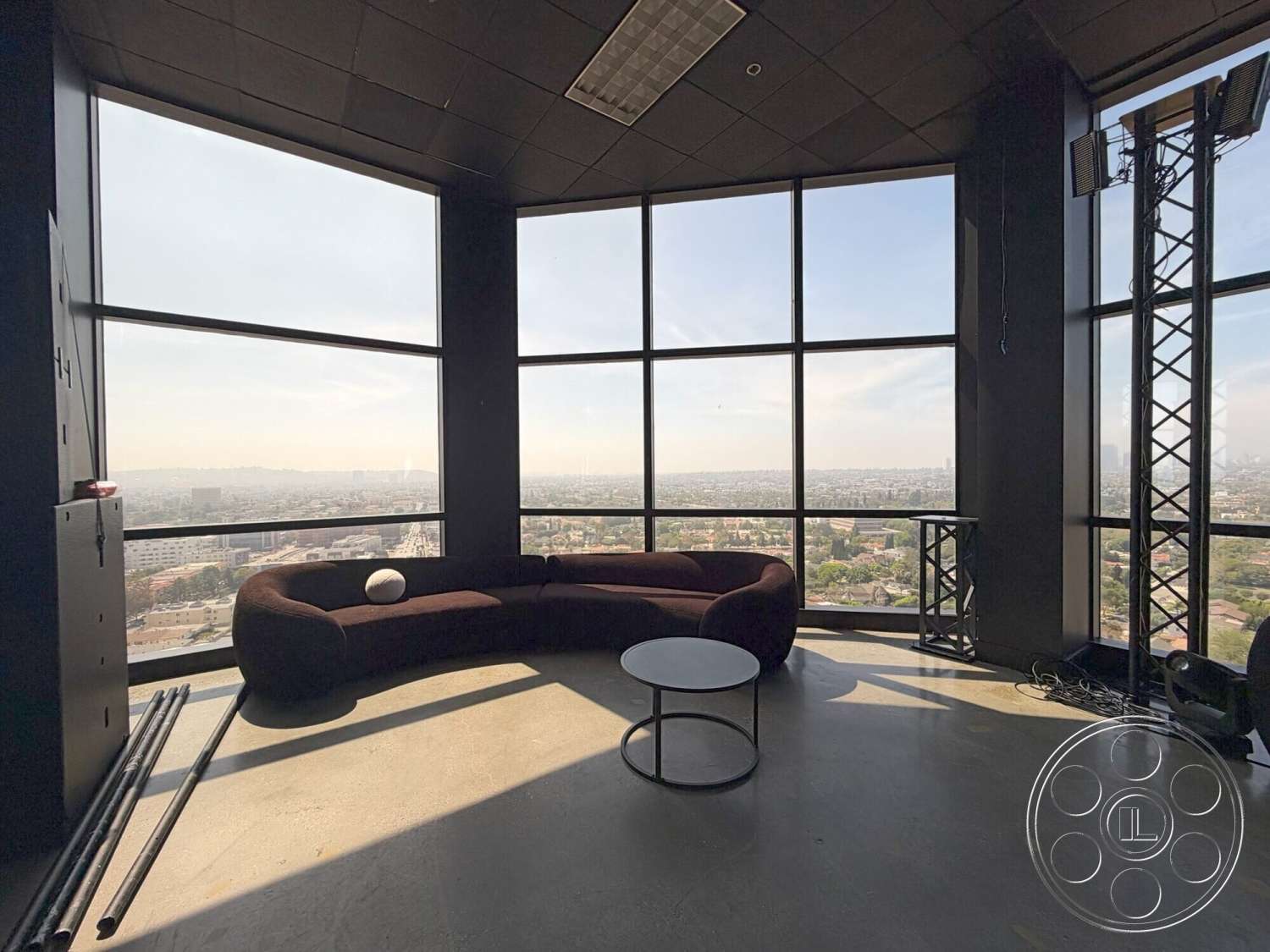 Wilshire Penthouse - minimalist design, open floor plan, concrete floor, modern coffee table, floor-to-ceiling windows, panoramic city view, curved sofa, black ceiling tiles