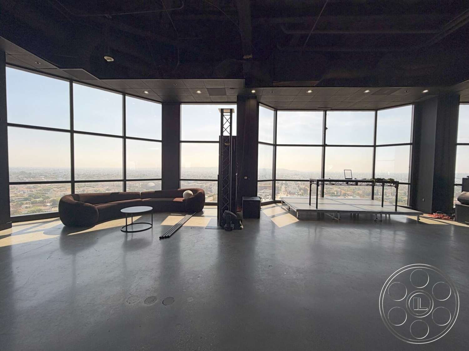 Wilshire Penthouse - open floor plan, concrete flooring, modern design elements, ambient lighting, interior space, metal framework, industrial style, floor-to-ceiling windows, city skyline view, minimalist coffee table, curved sectional sofa, black painted ceiling