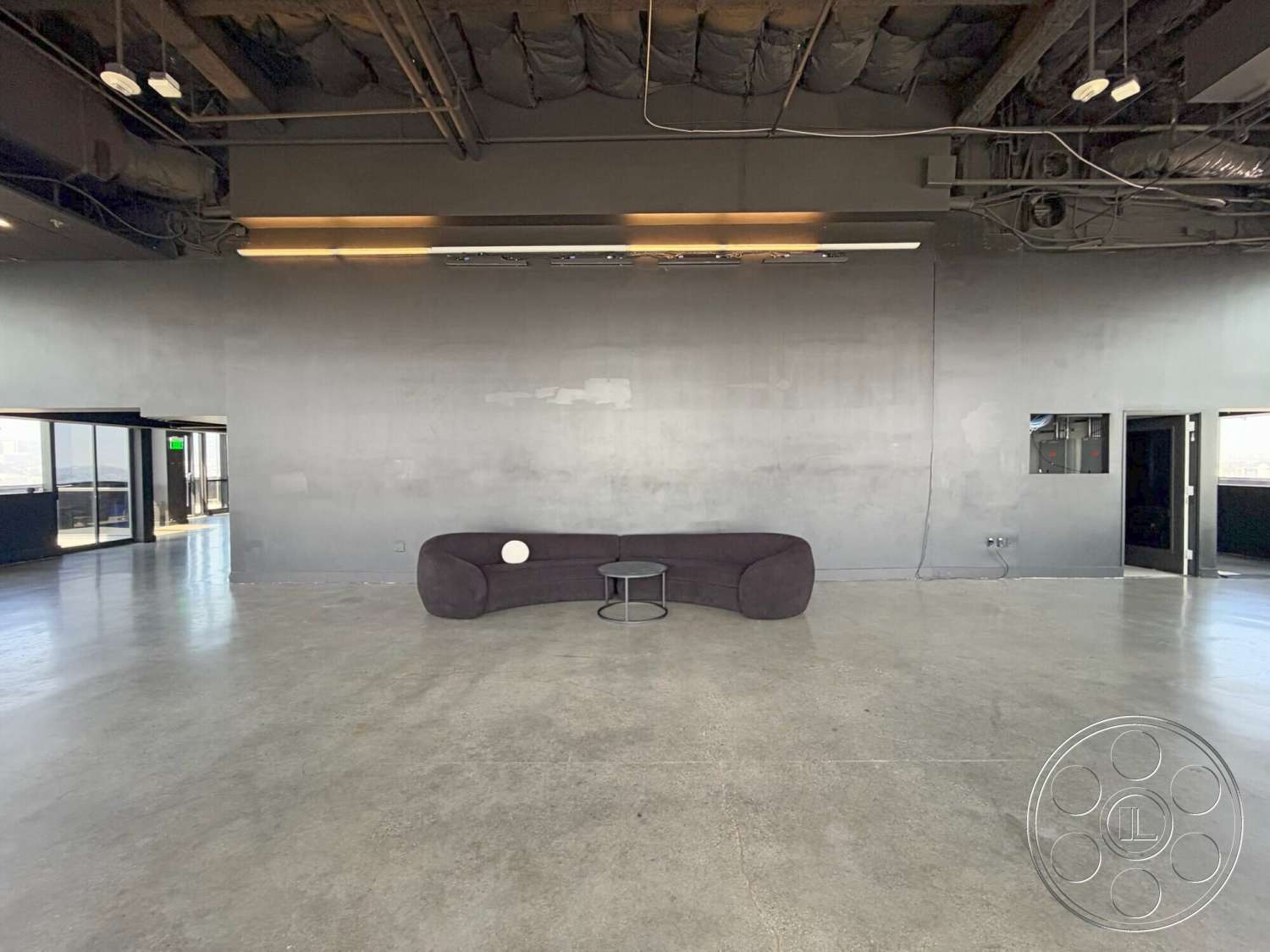 Wilshire Penthouse - concrete walls, floor-to-ceiling windows, metal coffee table, minimalist interior, exposed concrete flooring, industrial ceiling with exposed ductwork, modern curved couch