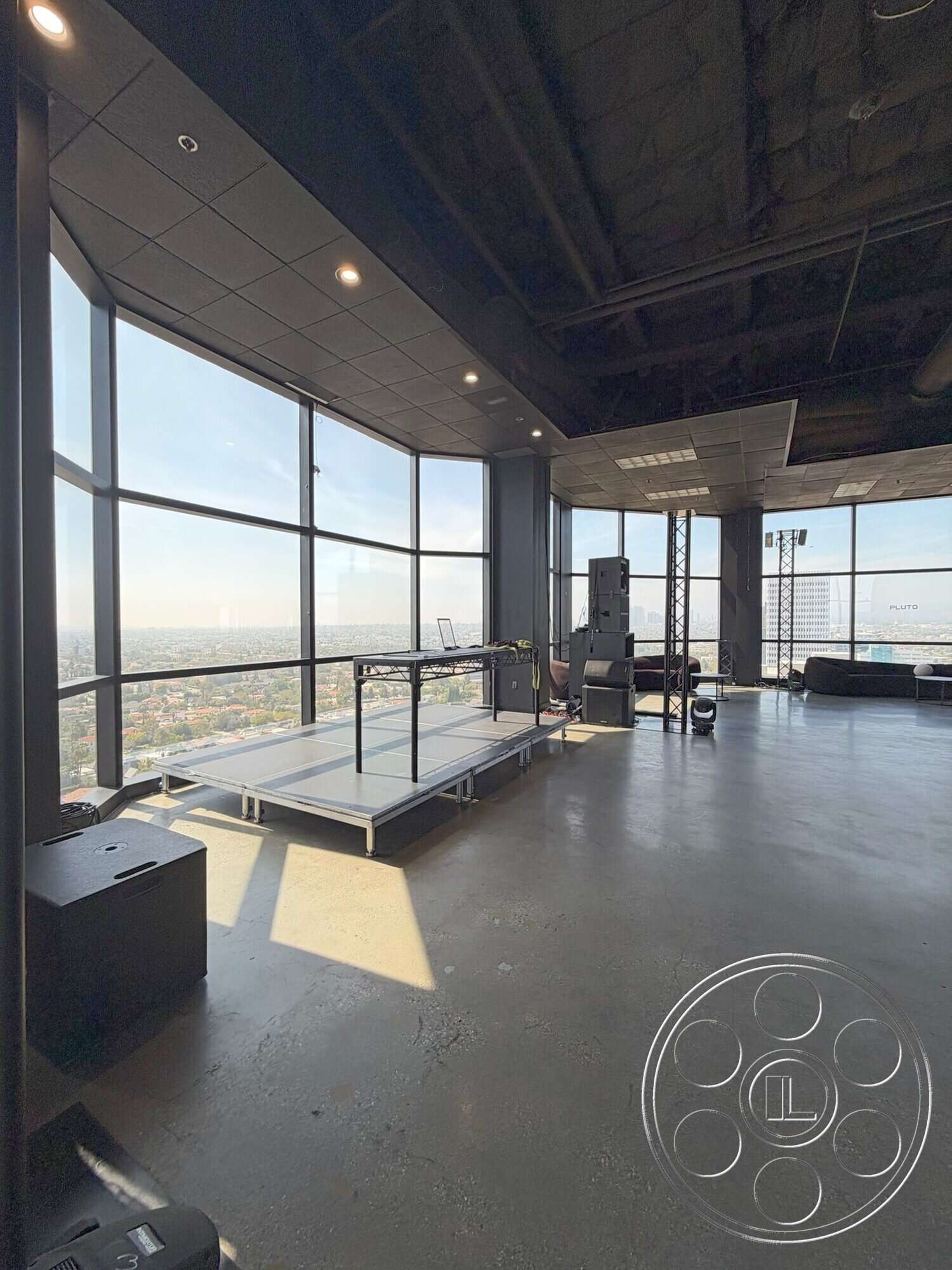 Wilshire Penthouse - open floor plan, polished concrete flooring, track lighting, minimalist furniture, floor-to-ceiling windows, urban skyline view, black acoustic ceiling tiles, industrial ceiling details, modern workout space, multi-purpose fitness area