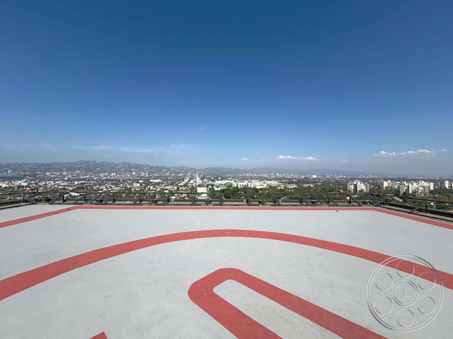 Wilshire Penthouse - exterior, urban skyline view, mountain backdrop, flat roof design, red painted markings, concrete helicopter pad