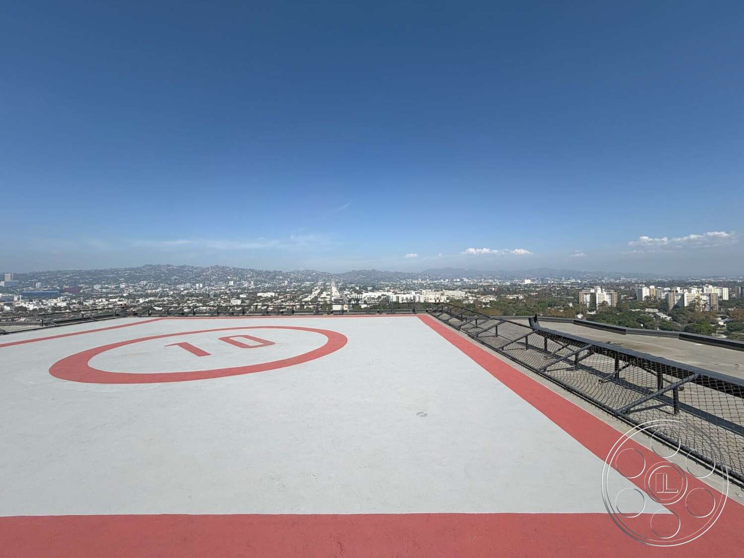 Wilshire Penthouse - exterior, mountain backdrop, open sky, metal safety railing, flat rooftop, urban city skyline view, red painted helipad markings, helipad concrete surface