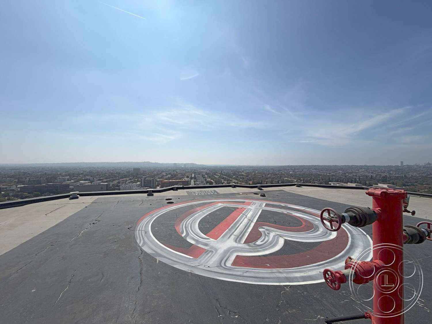 Wilshire Penthouse - urban landscape, city skyline view, flat rooftop surface, gray asphalt surface, helicopter landing pad, roof-mounted fire hydrant, red and white painted markings, exterior rooftop environment