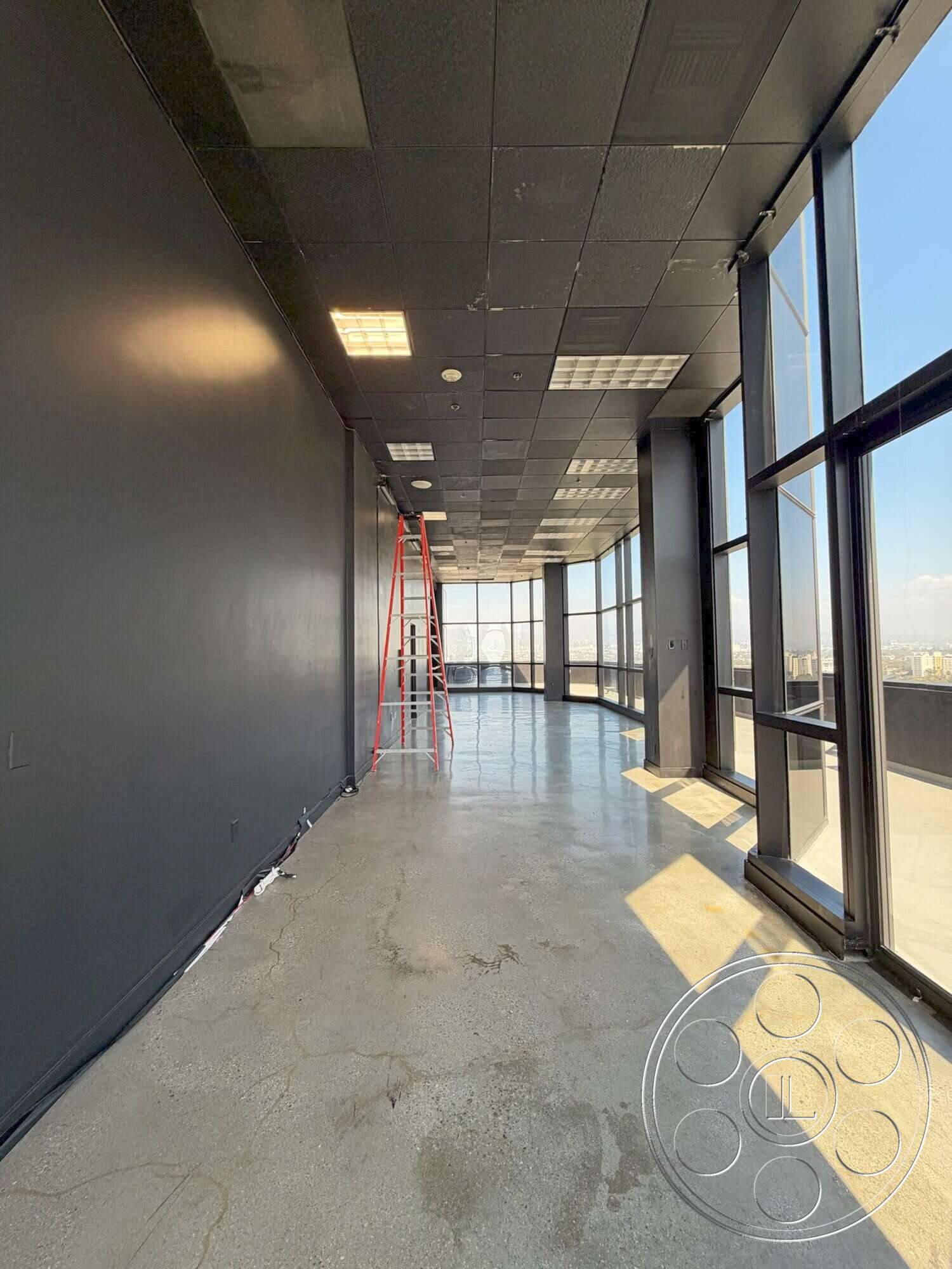 Wilshire Penthouse - polished concrete flooring, modern architectural style, large floor-to-ceiling windows, open office space, black painted walls, ceiling tiles