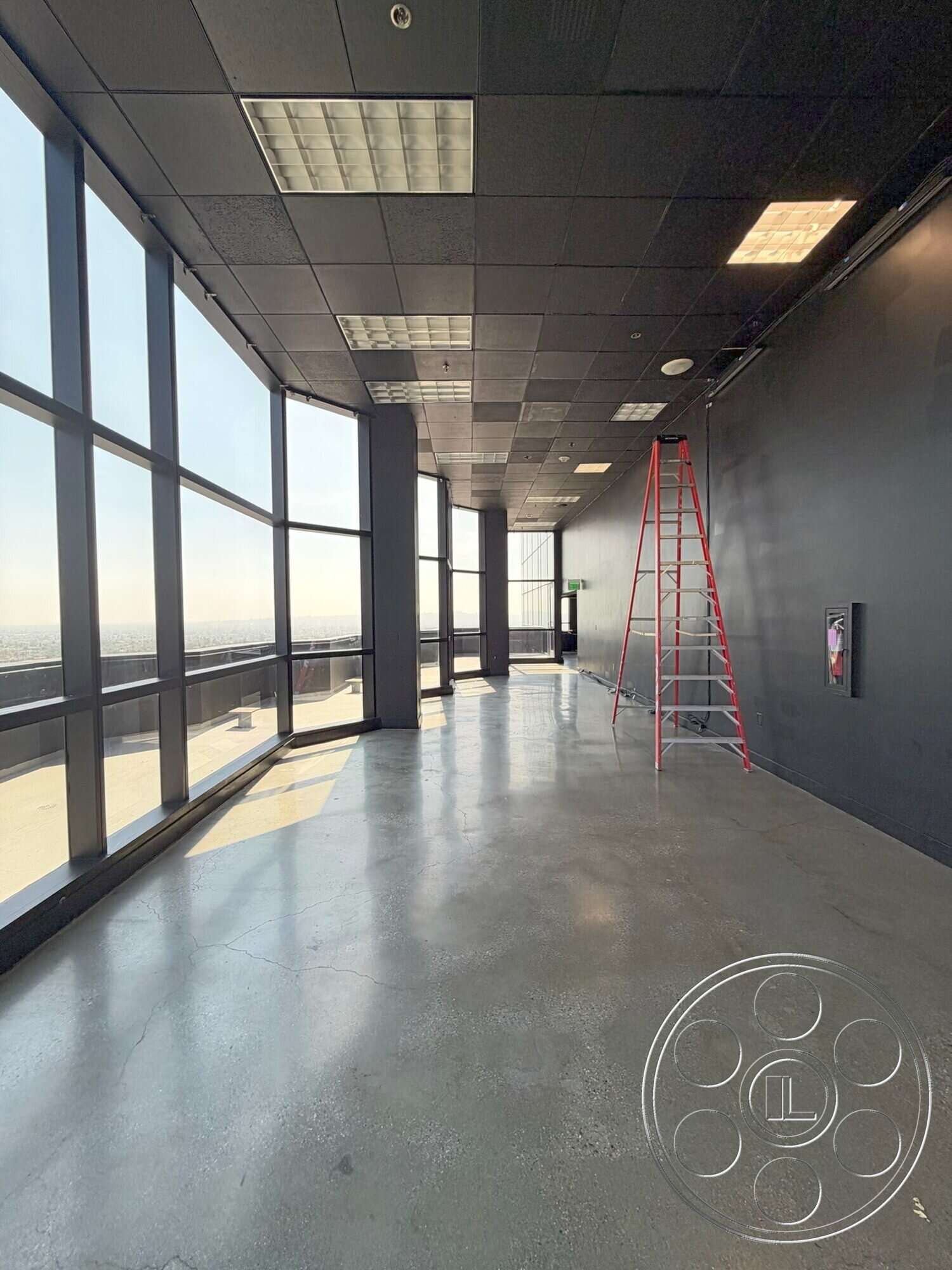 Wilshire Penthouse - high ceilings, concrete floor, floor-to-ceiling windows, industrial design elements, urban skyline view, modern office space, black acoustic ceiling tiles, temporary ladder