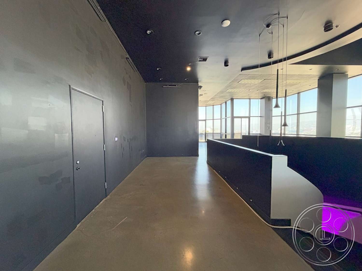 Wilshire Penthouse - polished concrete flooring, abstract wall art, modern pendant lighting, floor-to-ceiling windows, metal door, black painted walls, curved ceiling design, open layout space