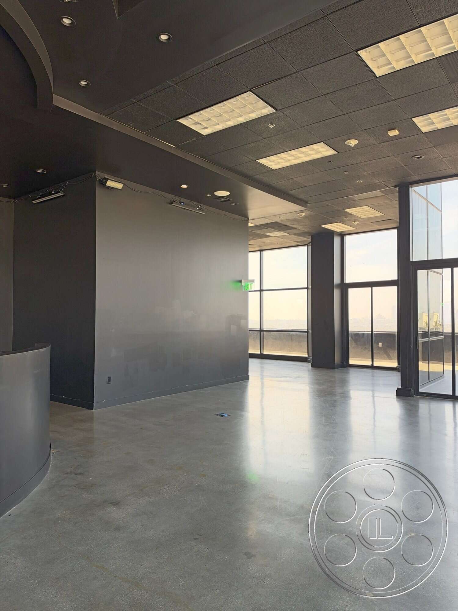 Wilshire Penthouse - open floor plan, polished concrete flooring, floor-to-ceiling windows, black painted walls, fluorescent lighting fixtures, acoustic tile ceiling, curved reception desk