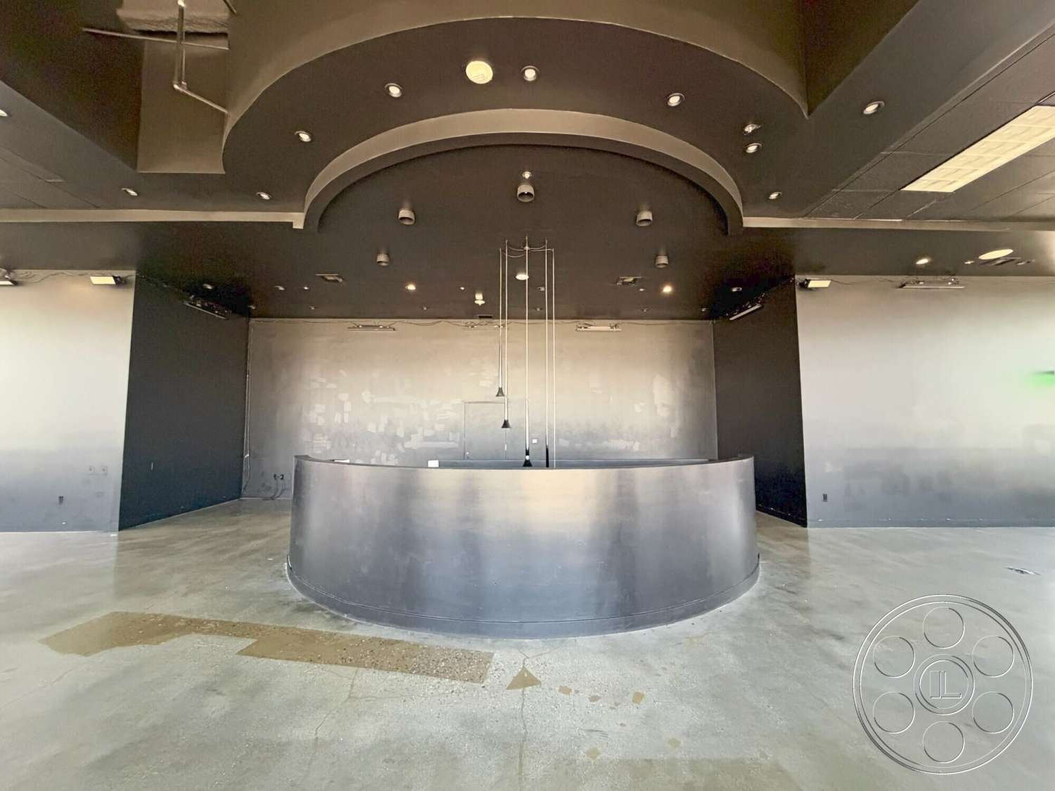 Wilshire Penthouse - polished concrete flooring, exposed ductwork, black painted walls, recessed lighting fixtures, smooth wall texture, curved reception desk, drop ceiling with circular shape