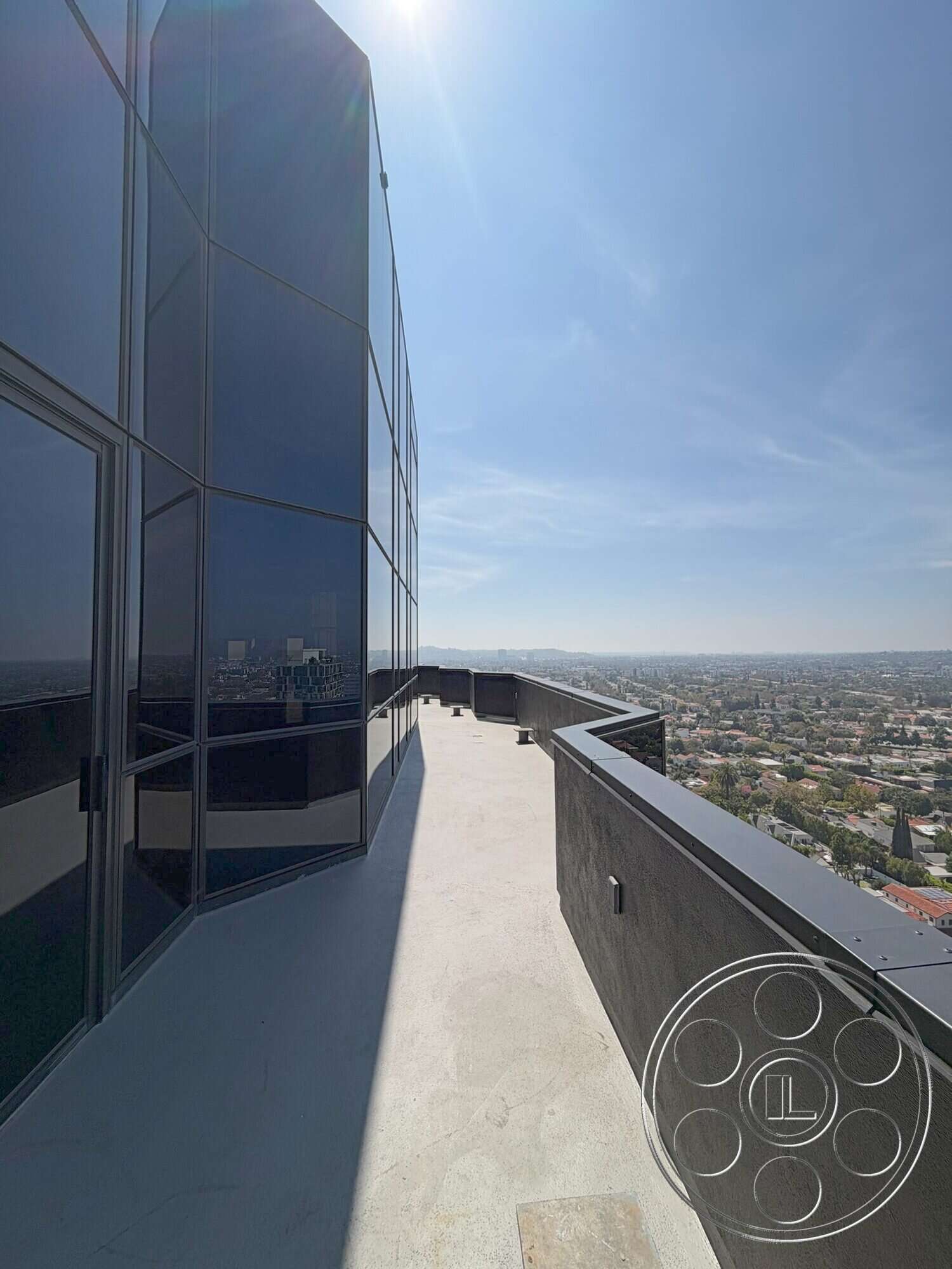 Wilshire Penthouse - exterior, metal railing, glass façade, modern architectural style, urban skyline view, high-rise building, flat roof design, concrete balcony flooring, curved balcony edge, black tinted windows
