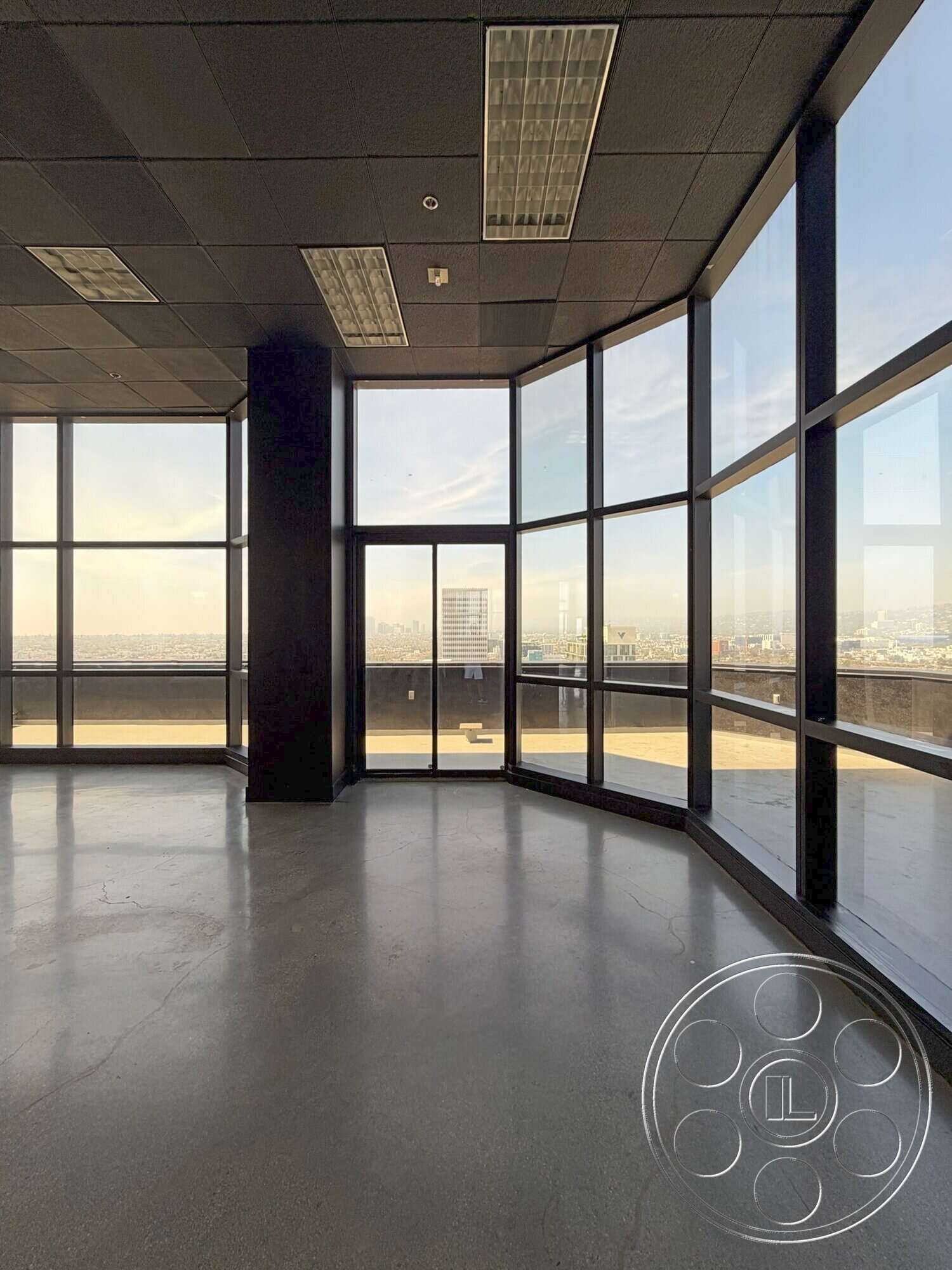 Wilshire Penthouse - polished concrete flooring, floor-to-ceiling windows, city skyline view, minimalist architectural style, commercial office space, black acoustic ceiling tiles, curved window wall