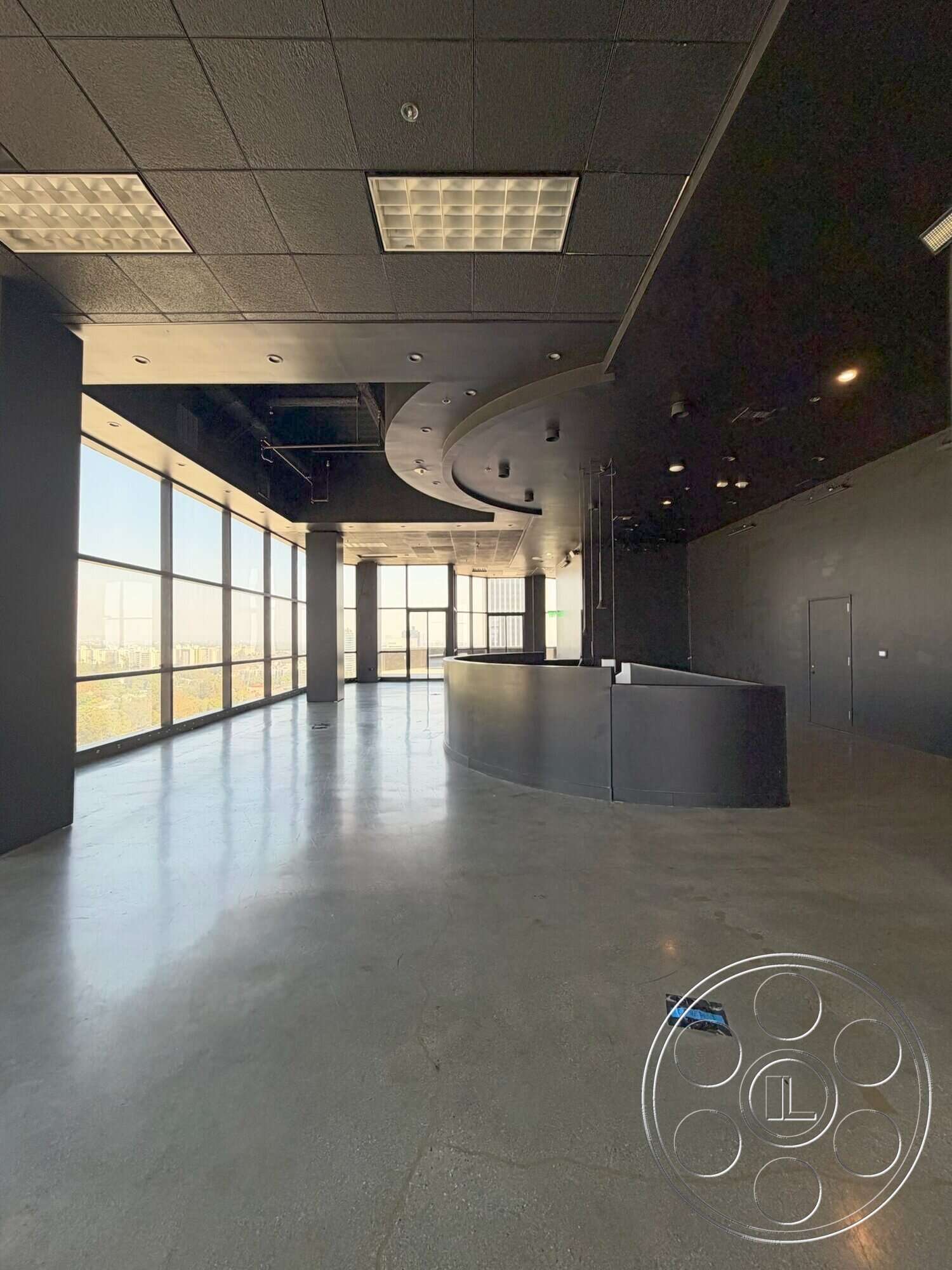 Wilshire Penthouse - open floor plan, polished concrete flooring, floor-to-ceiling windows, modern architectural design, industrial-style lighting fixtures, urban setting view, dark wall treatment, black drop ceiling, curved reception desk