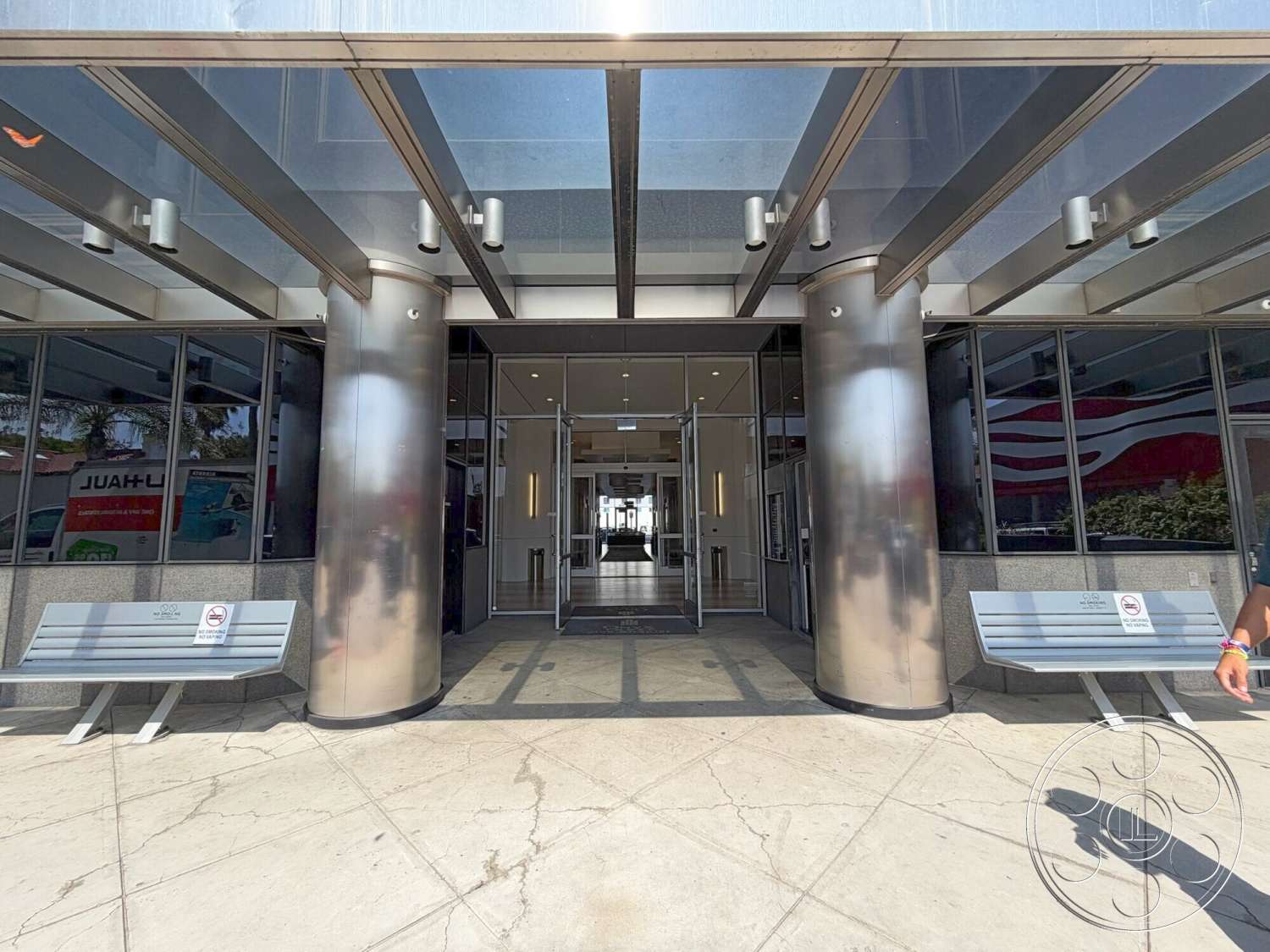 Wilshire Penthouse - exterior, concrete flooring, floor-to-ceiling windows, modern architectural style, glass entrance doors, stainless steel columns, textured stone wall cladding, overhead glass canopy, built-in concrete bench seating, open lobby entrance