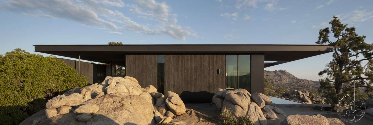 Palm Springs 110 - exterior, contemporary design, large glass windows, minimalist architecture, black wooden siding, surrounding vegetation, flat roof design, mountain view setting, overhanging roof eaves, natural stone base, rocky landscape