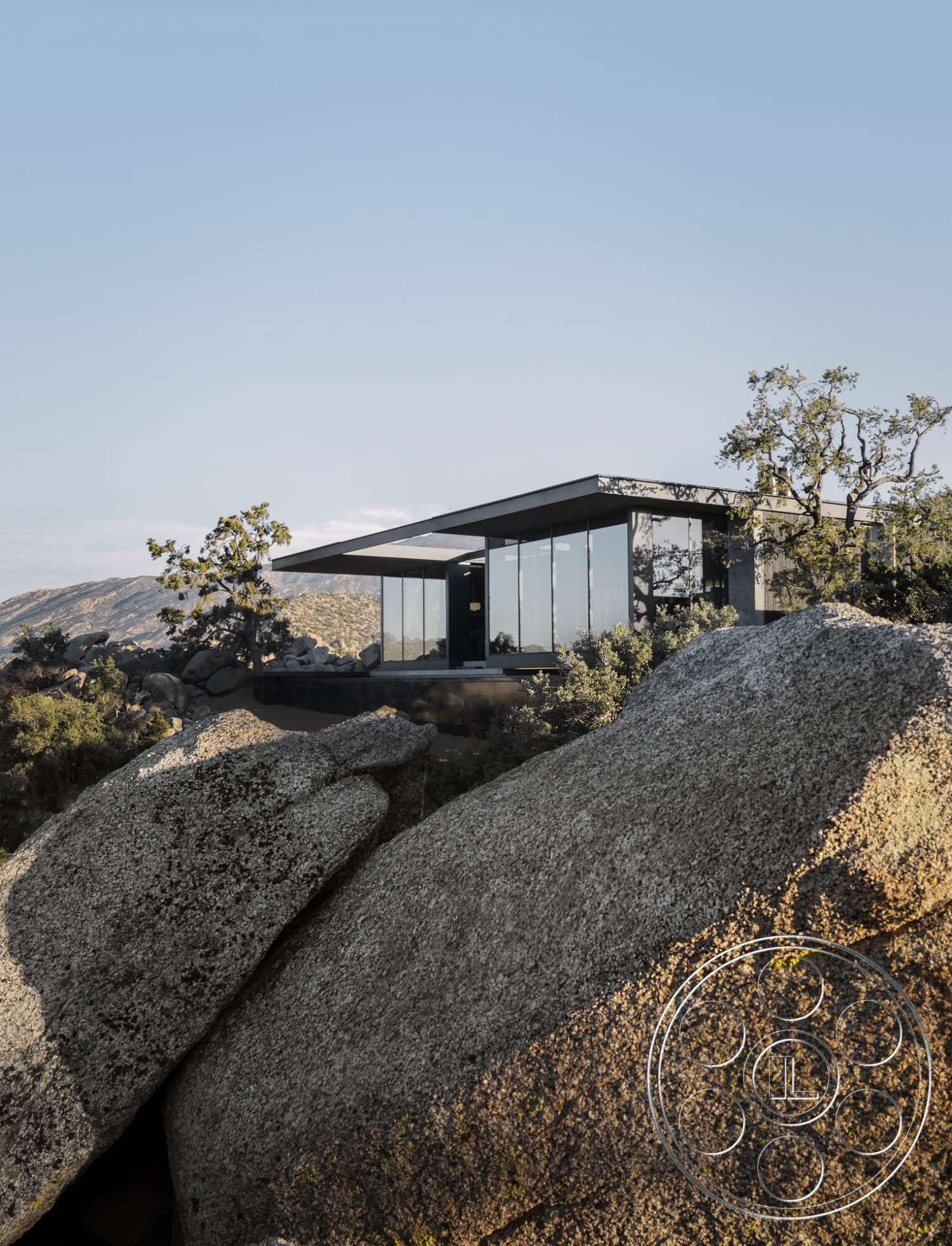 Palm Springs 110 - exterior, flat roof, open floor plan, glass facade, modern architectural style, large floor-to-ceiling windows, mountainous background, natural stone boulders, steel roof, minimized landscaping, scenic desert setting