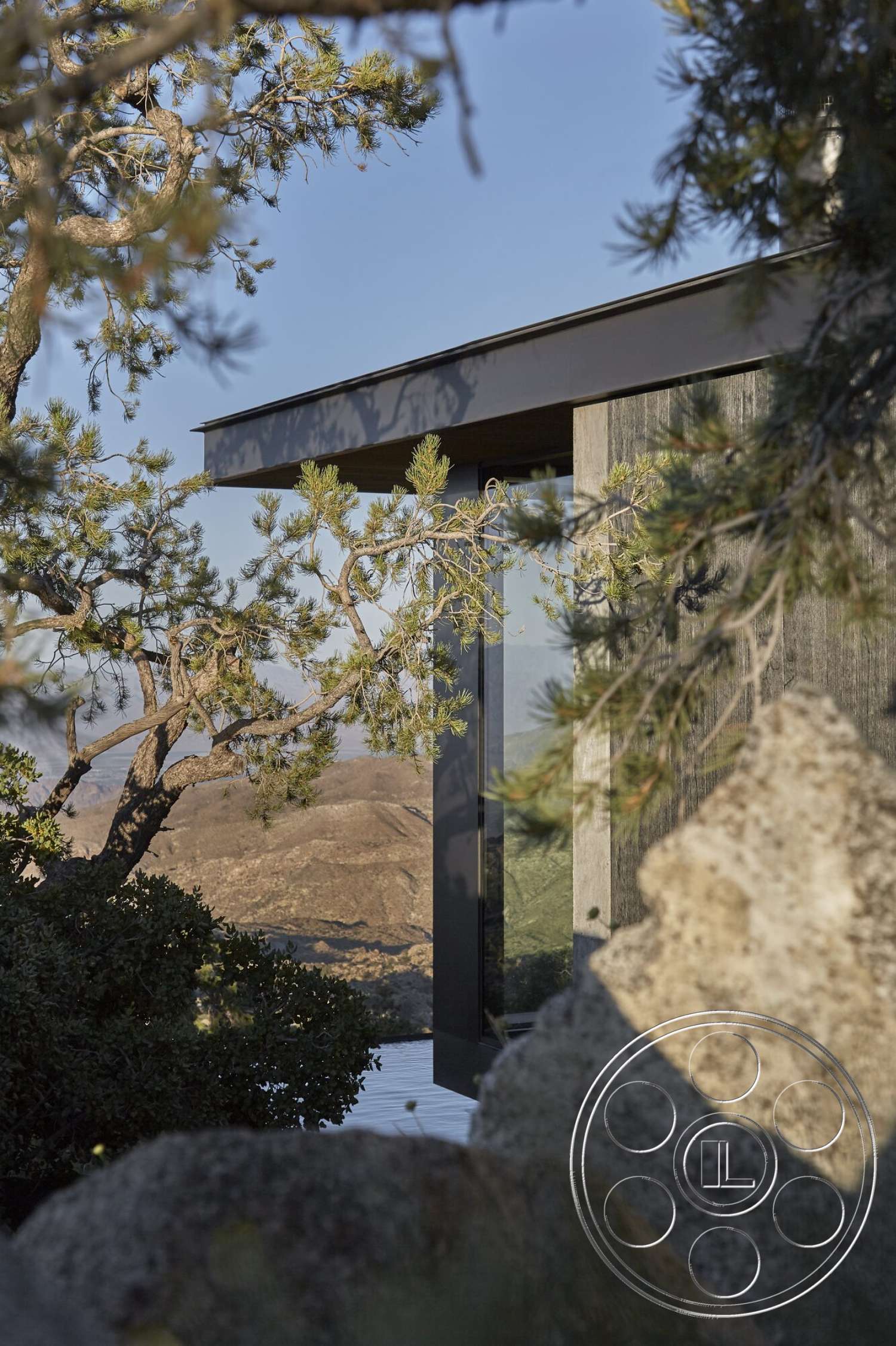 Palm Springs 110 - exterior, open terrace, large floor-to-ceiling windows, black metal roof, contemporary architectural style, mountain view setting, wood siding exterior, natural boulder landscaping, surrounding forest vegetation