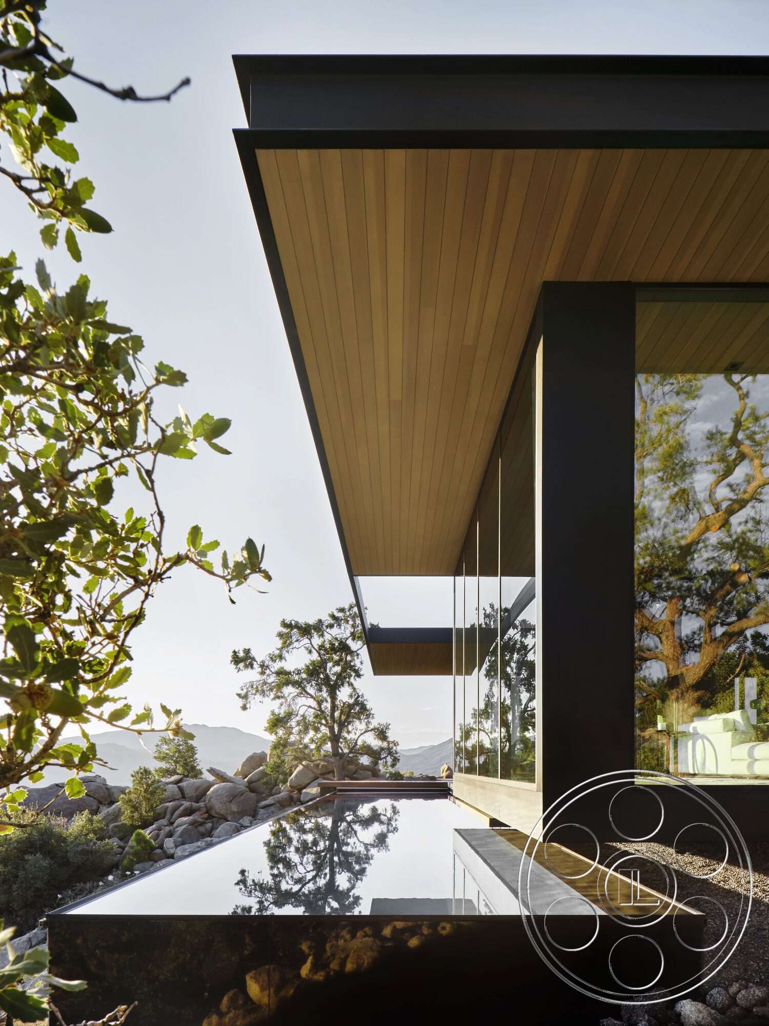 Palm Springs 110 - exterior, large glass windows, modern architectural style, mountain view, metal roof, smooth stone patio, reflective water feature, minimalist facade, overhanging roof, wood soffit ceiling, landscaped rocky garden