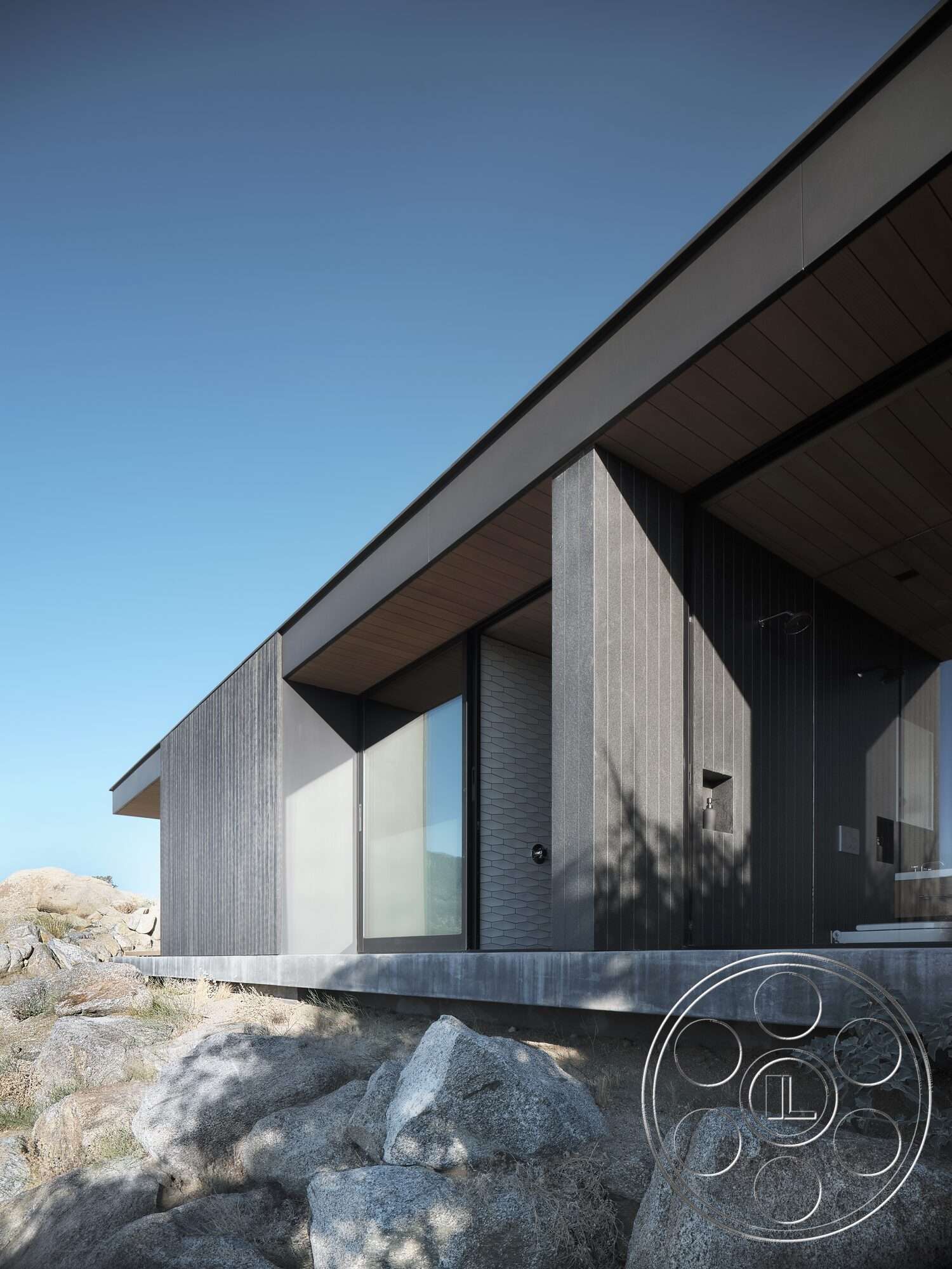Palm Springs 110 - exterior, modern architectural style, stone landscaping, flat roof design, minimalist facade, large floor-to-ceiling glass windows, wood-finished overhang, textured vertical wood siding, concrete foundation wall